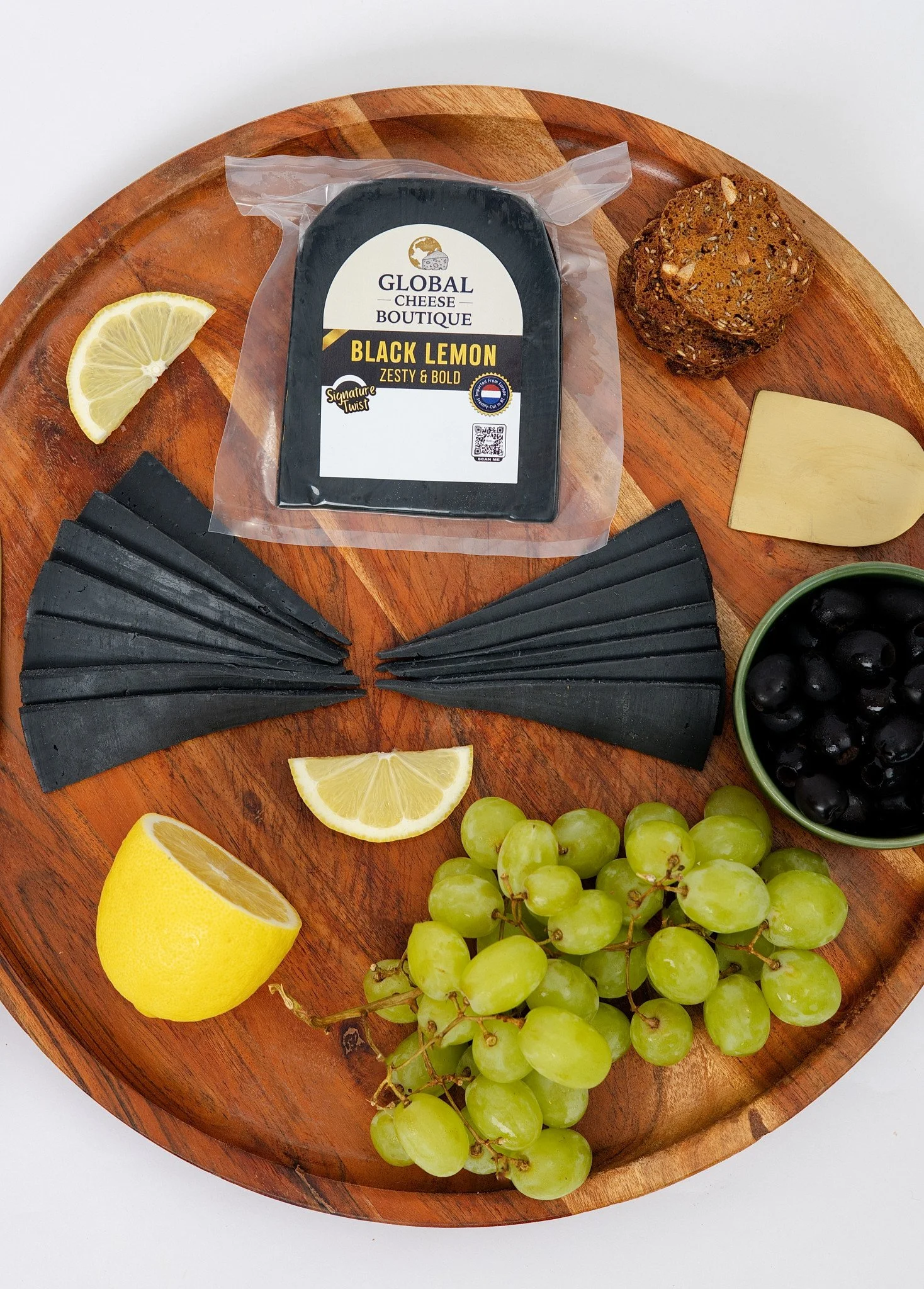 Black Lemon Gouda 180 g, sealed pack and slices on a round board with grapes and lemon