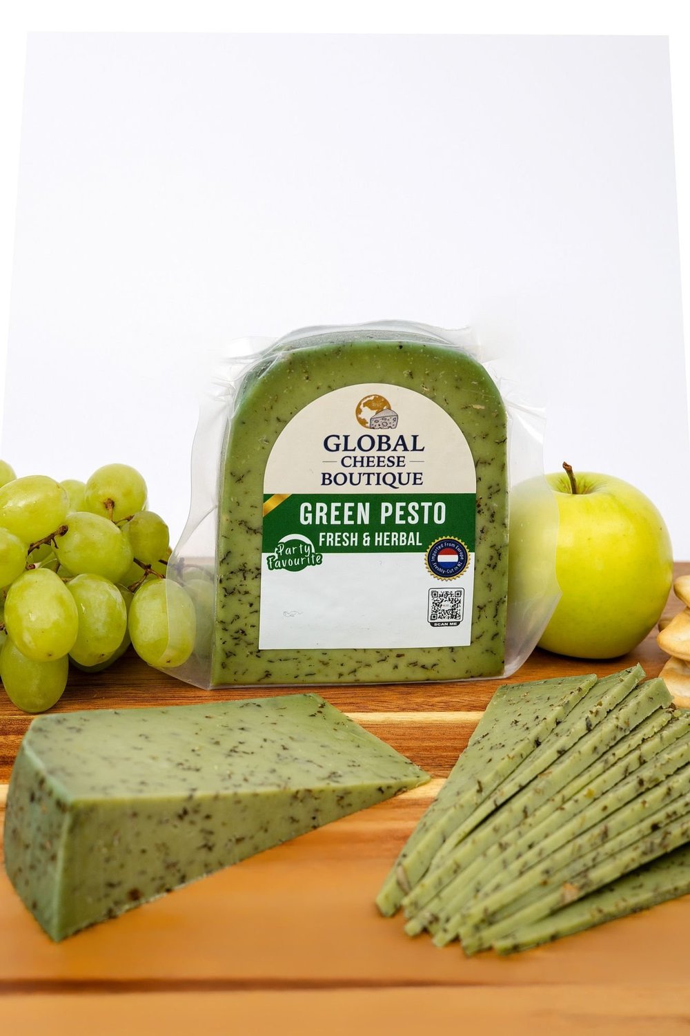 Green Pesto Gouda pack with a wedge, slices, grapes and an apple on a wooden board
