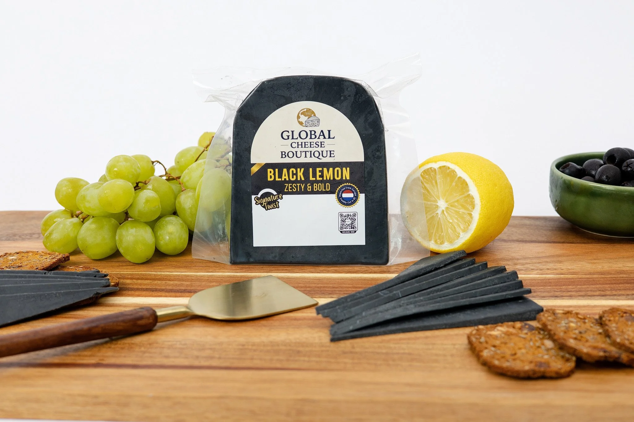 Black Lemon Gouda 180 g, sealed pack and slices on a board beside lemon