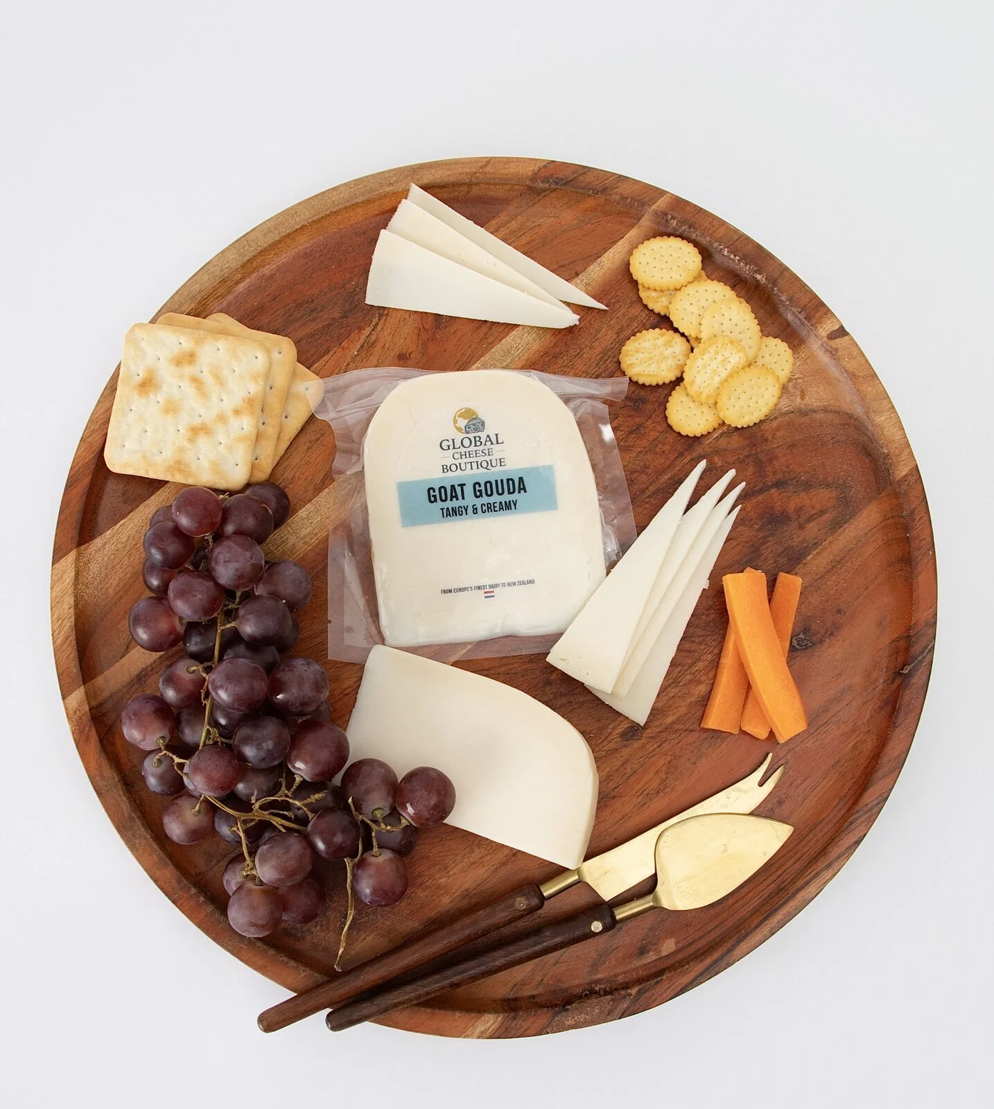 Overhead view of Goat Gouda with cheese slices, grapes, crackers and carrot sticks on a wooden board.