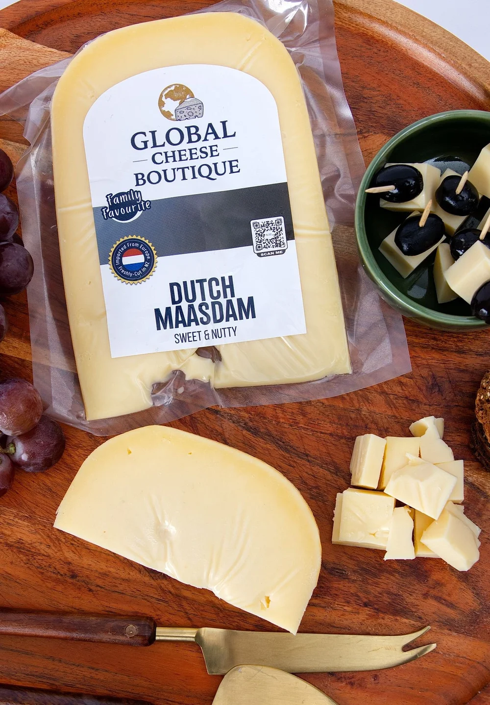 Dutch Maasdam pack with a cheese wedge, cubes, grapes and olives on a wooden serving board
