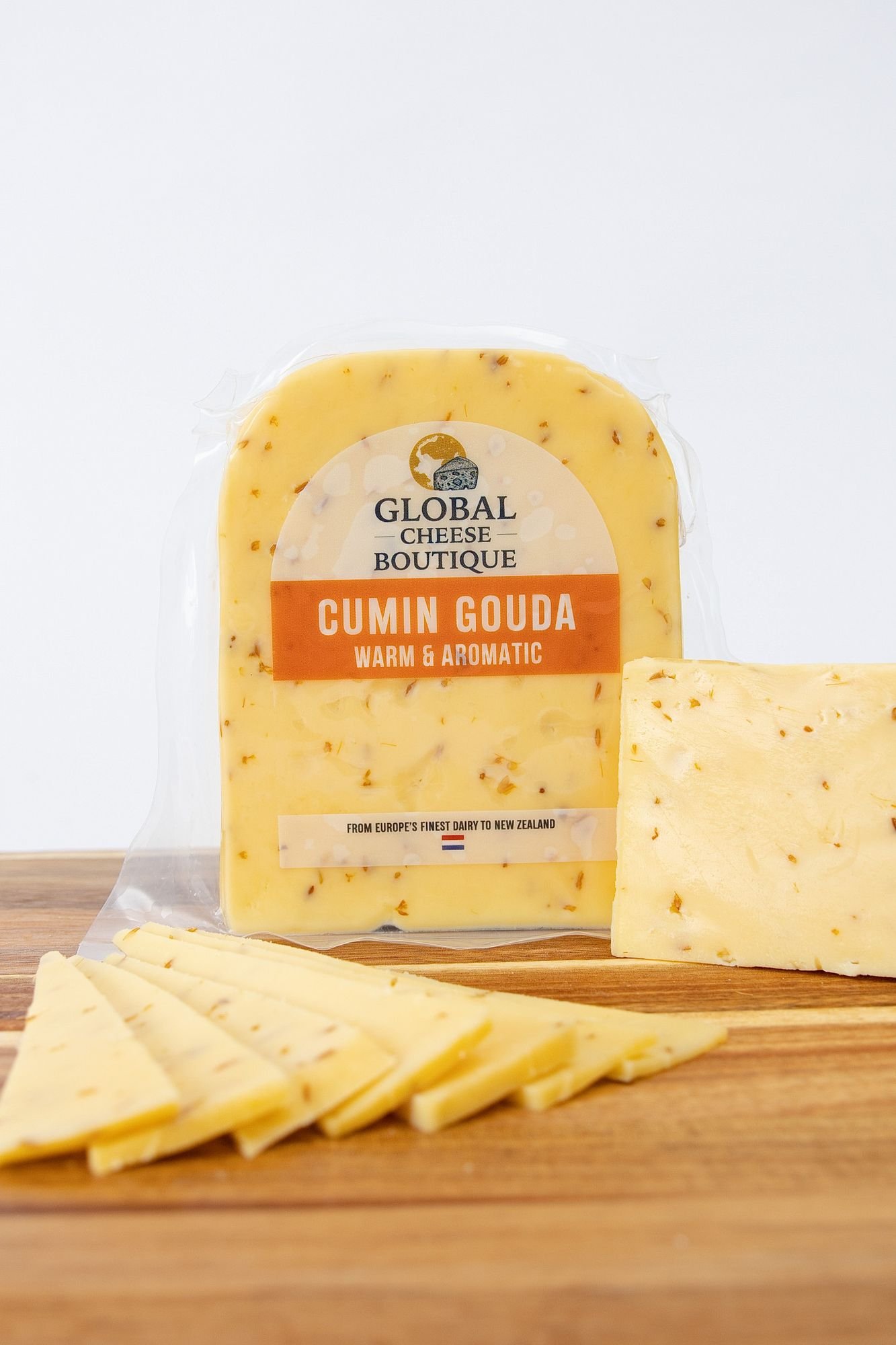 Cumin Gouda, sealed pack with a wedge and slices on a wooden board