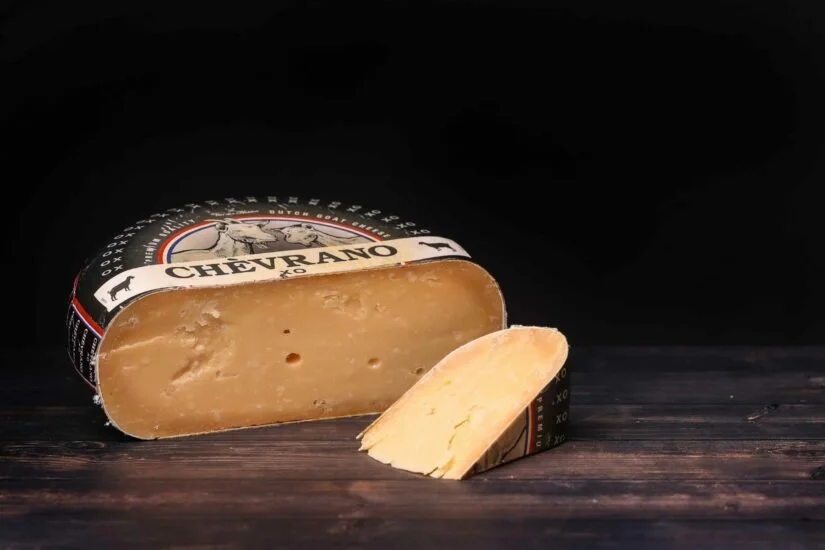 Block of Chevre Ano cheese with a slice cut and placed in front of it on a dark wooden surface.