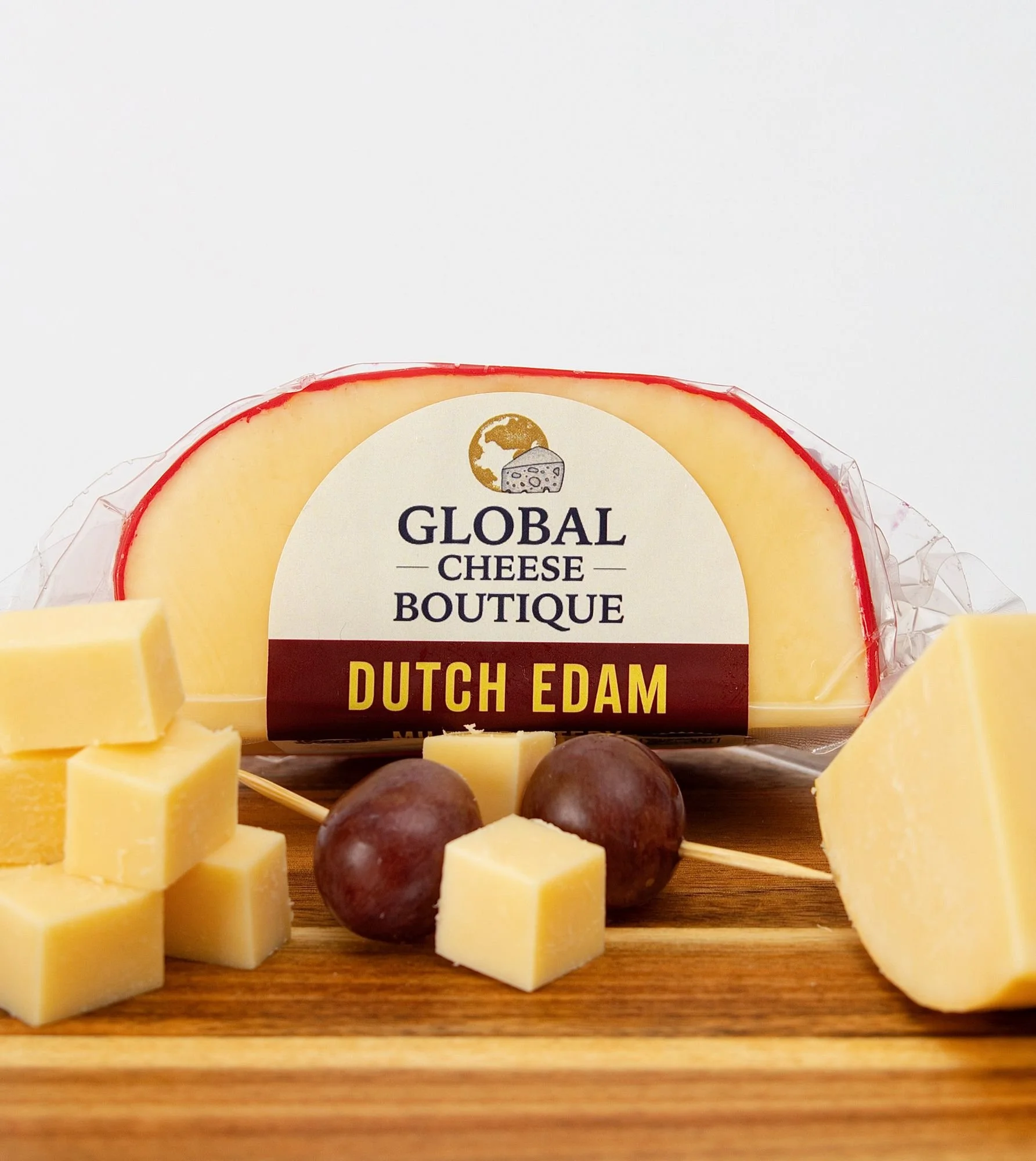 Dutch Edam, sealed pack with cut cheese, cubes and grapes on a wooden board