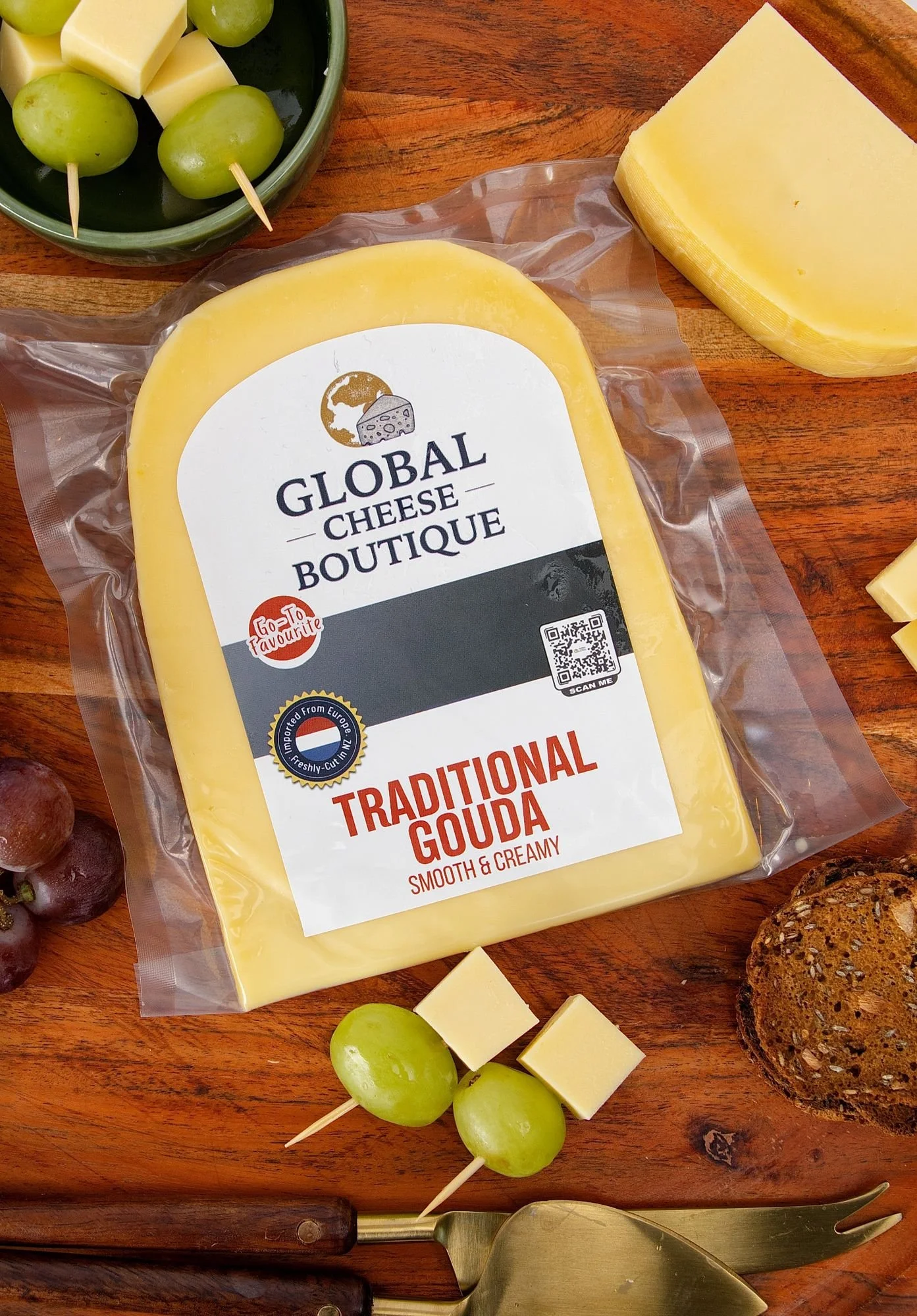 Traditional Gouda sealed pack with a wedge, cheese cubes, grapes and crackers on a wooden board
