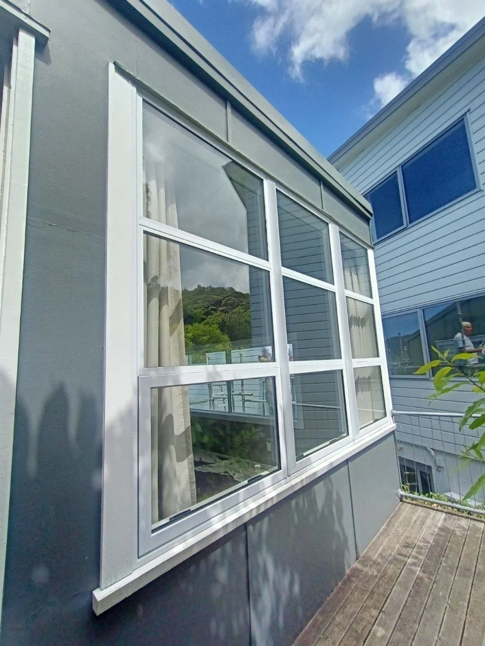 Exterior of a house with large windows, gray siding, and a wooden deck, with a partly cloudy sky above.
