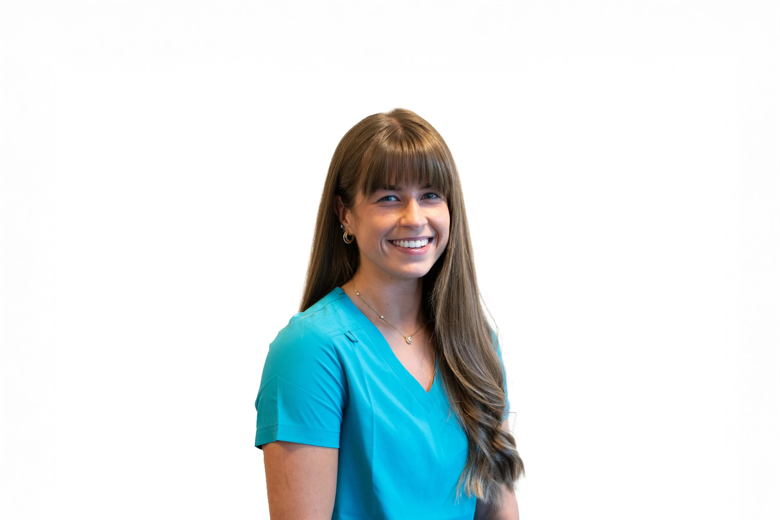 A young woman with long brown hair, wearing a turquoise scrub top, smiling, against a plain white background.
