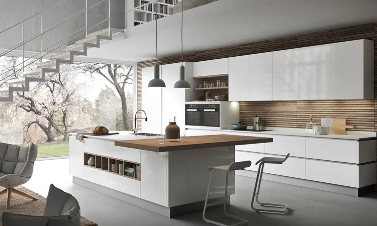 Modern kitchen with white cabinetry, wooden accents, and a large island with a wooden countertop, overlooking large windows with a view of trees outside.