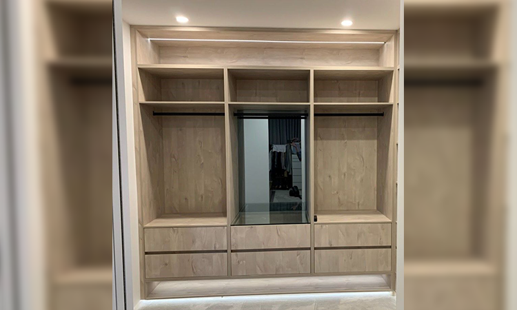 Empty wooden wardrobe with shelves, hanging rods, and a mirror in the center, in a well-lit room.