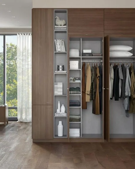 Modern bedroom closet with shelves and hanging space, containing folded clothes, shoes, and decorative items, adjacent to a window with white curtains.
