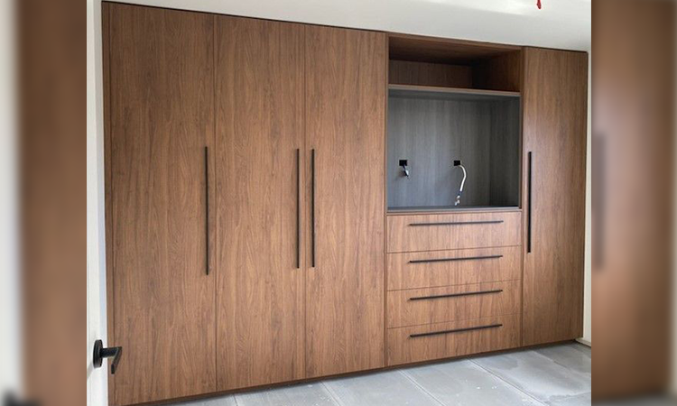 Wooden built-in cabinet or wardrobe with multiple doors and drawers, installed in a room with tiled flooring.