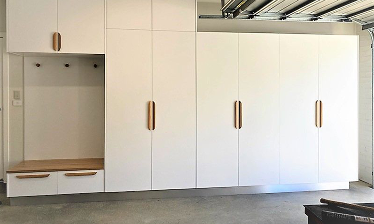Modern white storage cabinets in a garage with wooden handles and a small wooden bench with drawers