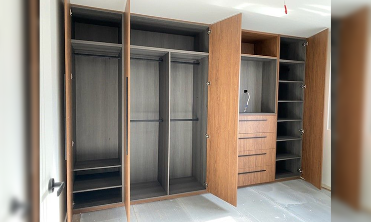 Open wooden closet cabinets with shelves and drawers in a room under construction.
