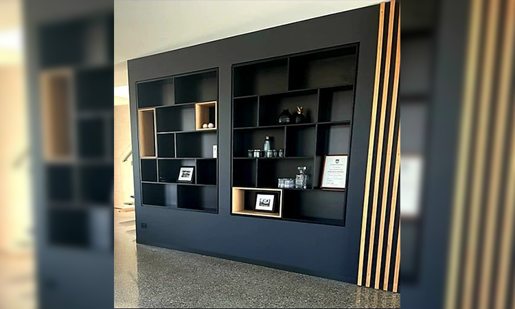 A black wall with built-in rectangular shelving units, some with decorative items, framed photos, and documents inside. The right side of the wall features wooden vertical slats.
