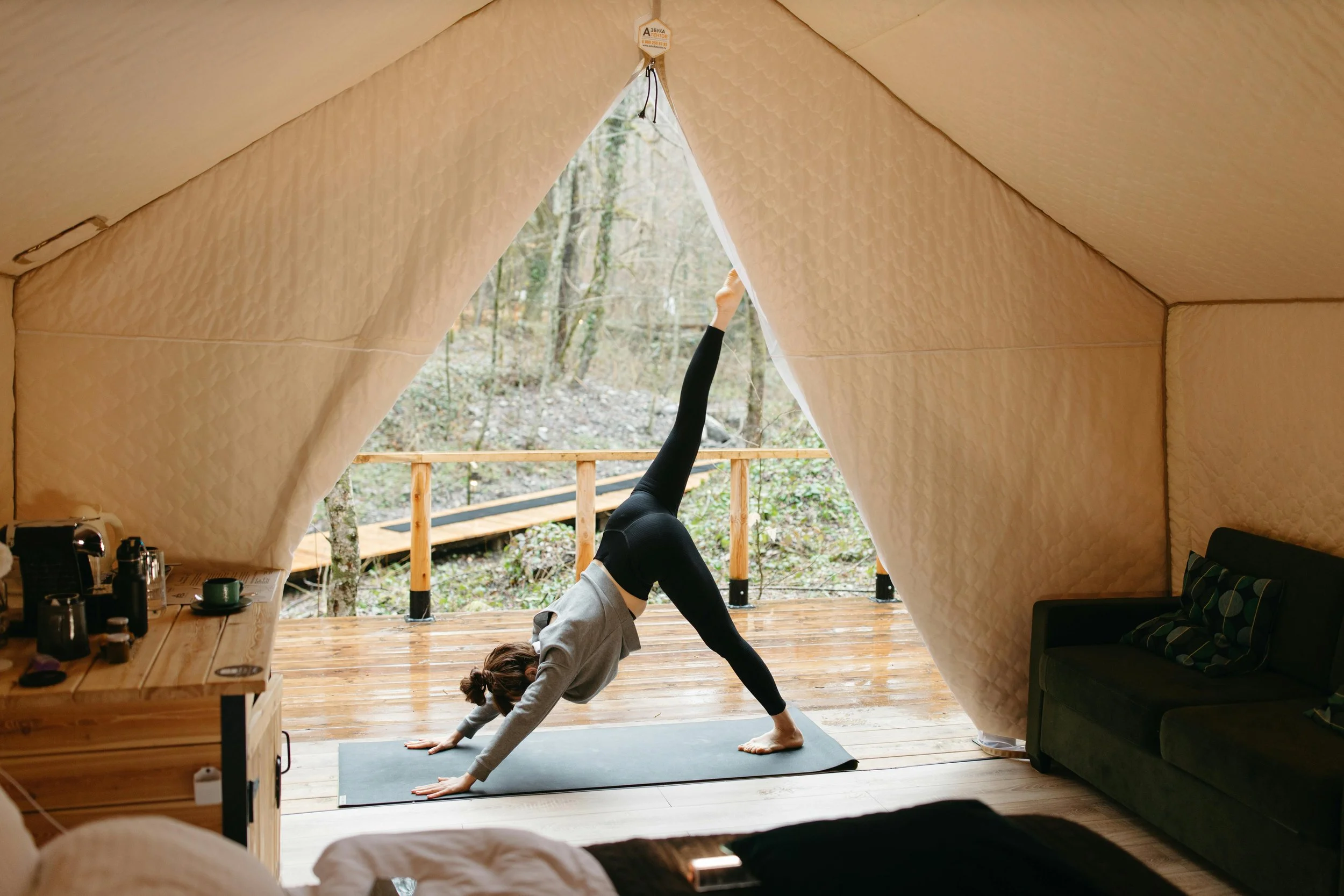 A person practicing yoga in a tent with an open front, facing a wooded outdoor area.