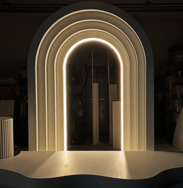 Modern illuminated decorative structure with multiple arch-shaped layers and LED lighting, set against a dark background.