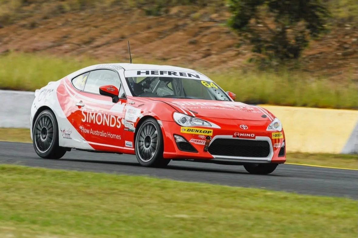 Red and white race car with sponsorship decals, driving on a race track.