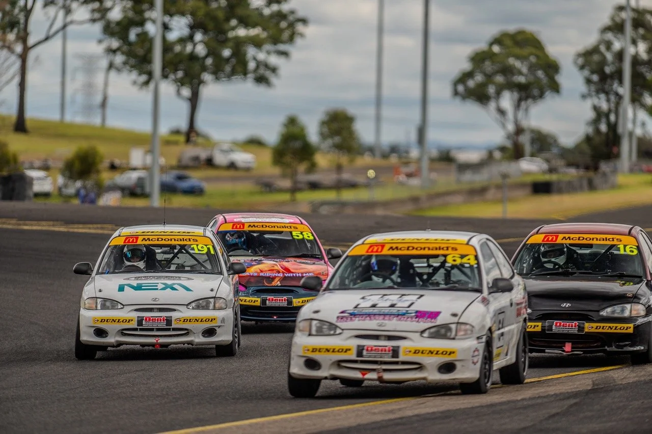 Race cars on a track competing in a race, with four cars visible in the image, navigating a curve during daytime.