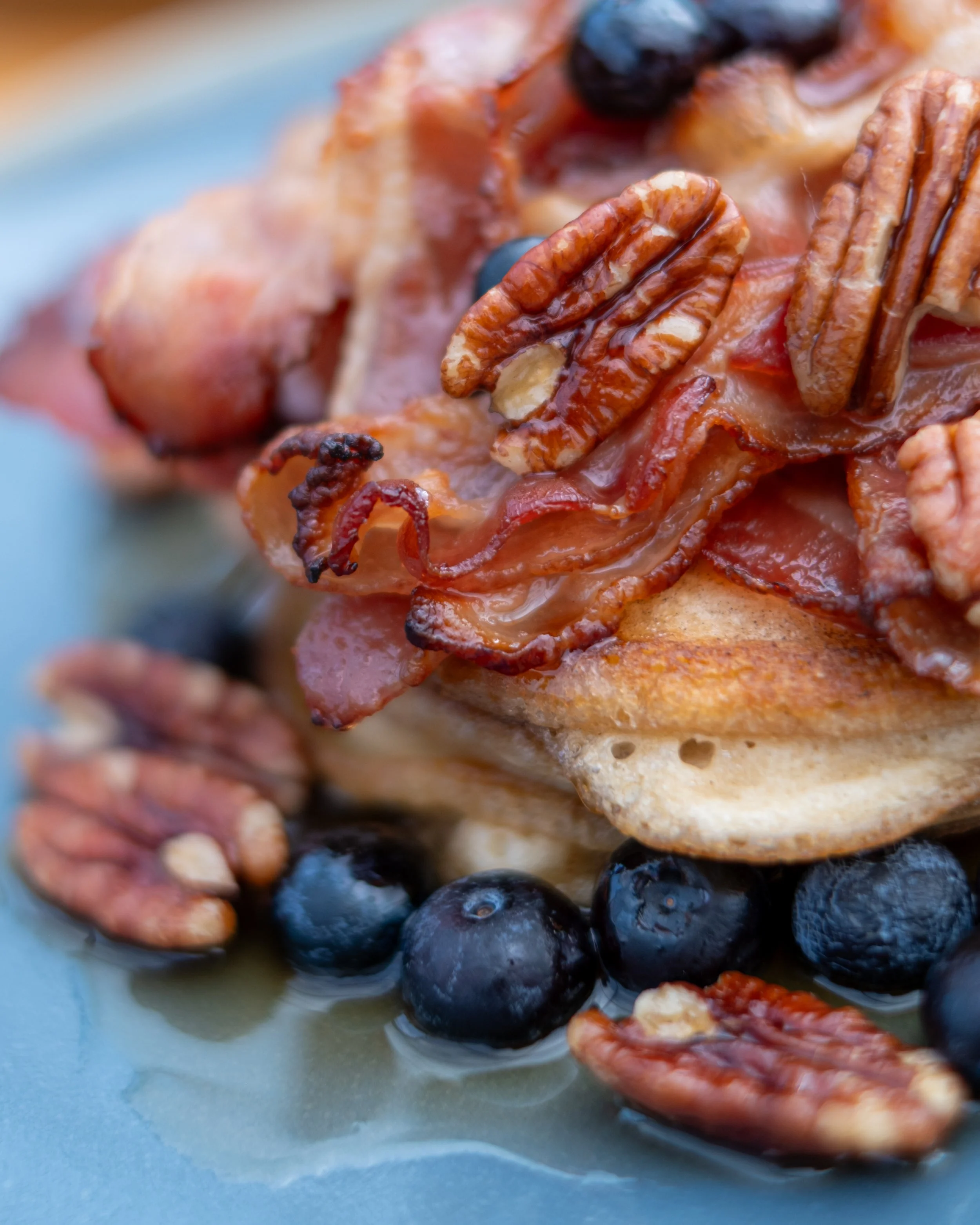 Close-up of a breakfast dish with bacon, blueberries, and pecans on a blue plate Blackpit Café