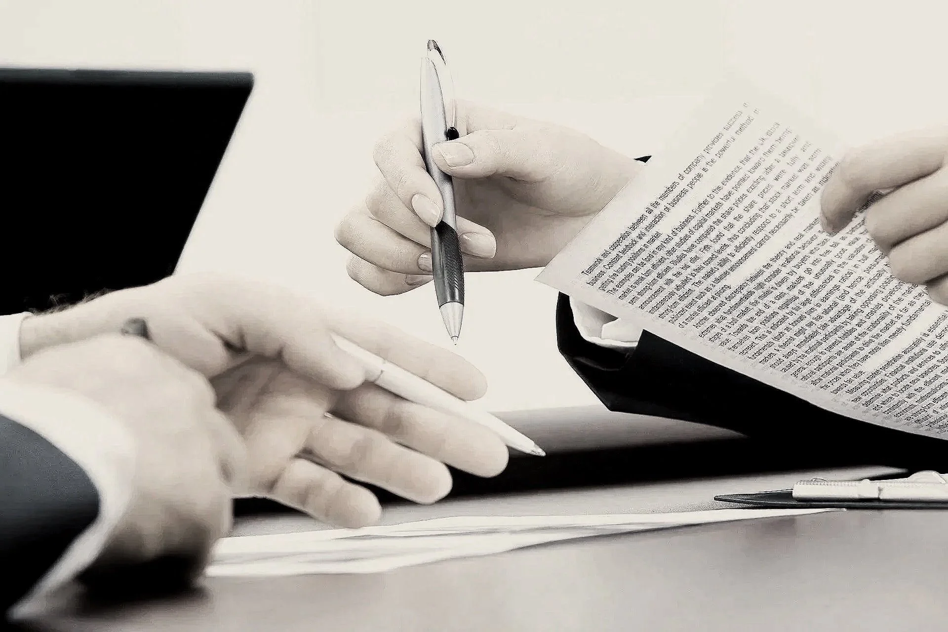 Two people engaged in a discussion, with one holding a smartphone and the other holding a pen and some papers, on a desk with a pen nearby.