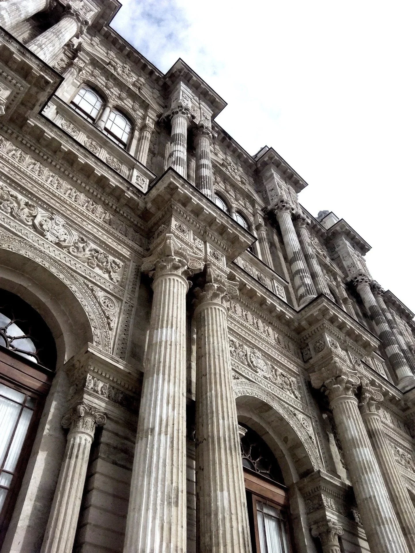 Close-up view of a historic building with ornate architectural details, tall Corinthian columns, decorative carvings, and arched windows, taken from a low angle looking up.
