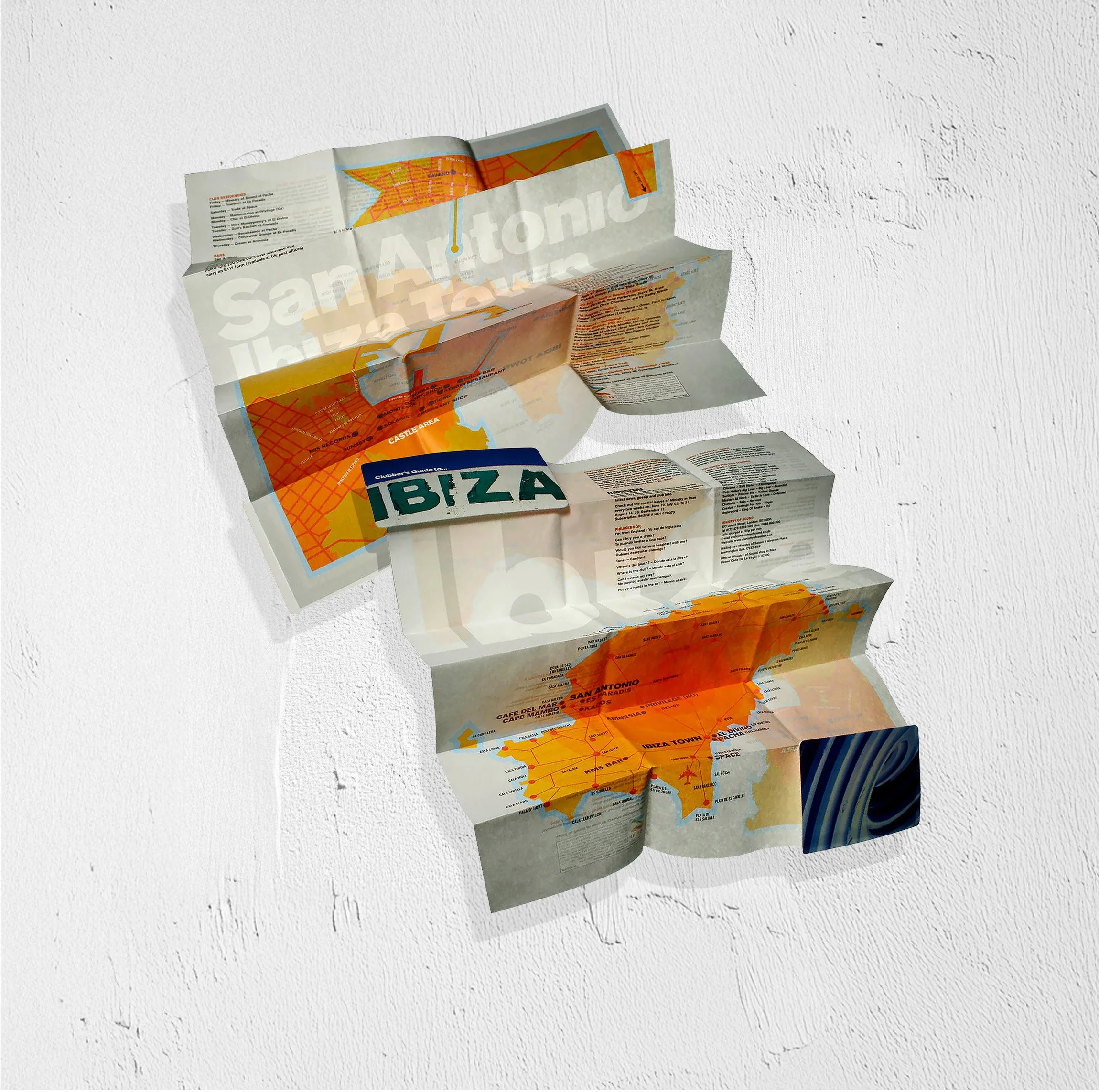 Folded map of Ibiza with highlighted areas and text, leaning against a white textured wall.