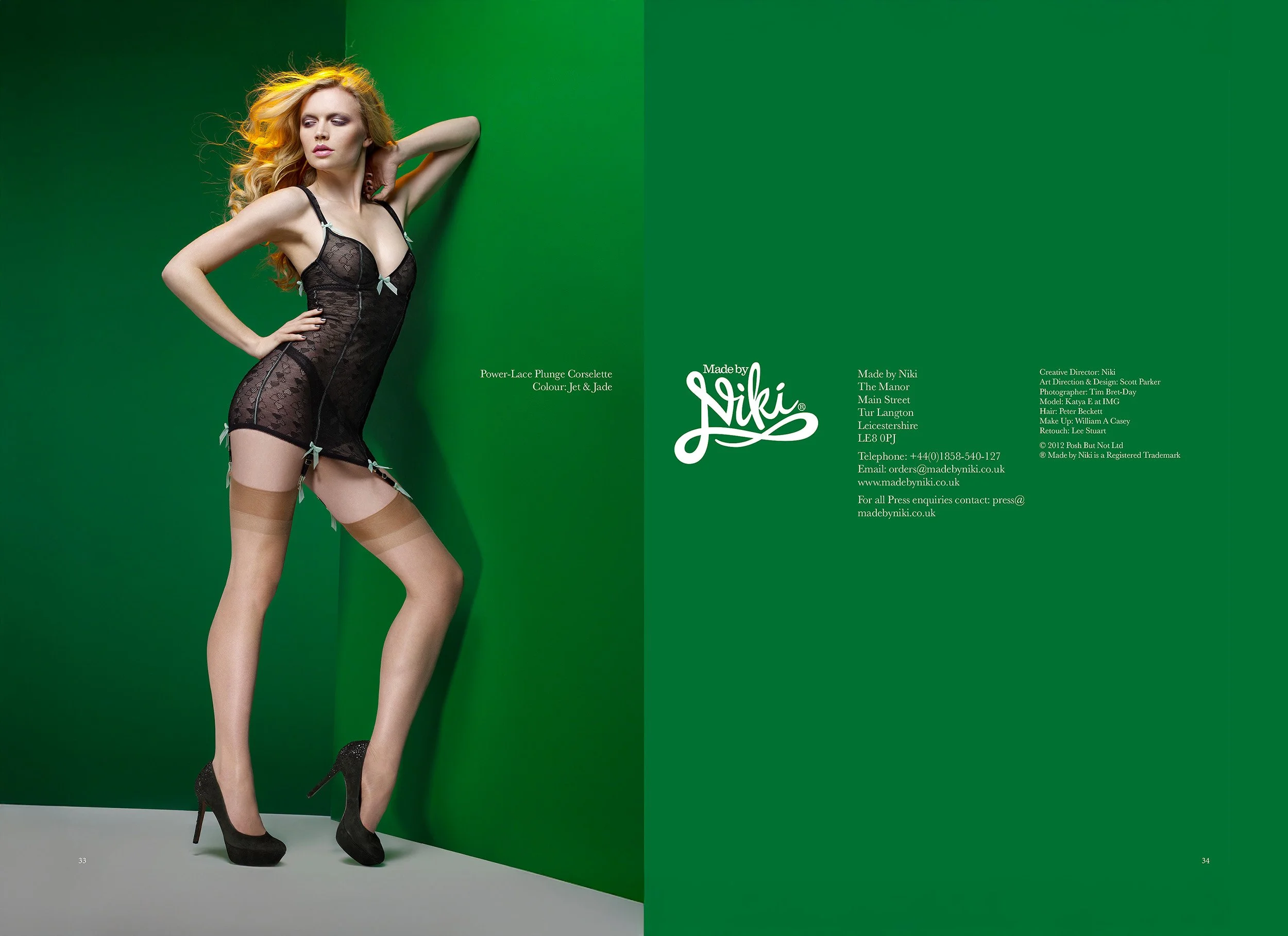A woman with curly blonde hair wearing black lace lingerie, beige thigh-high stockings, and black high heels, standing against a green background.