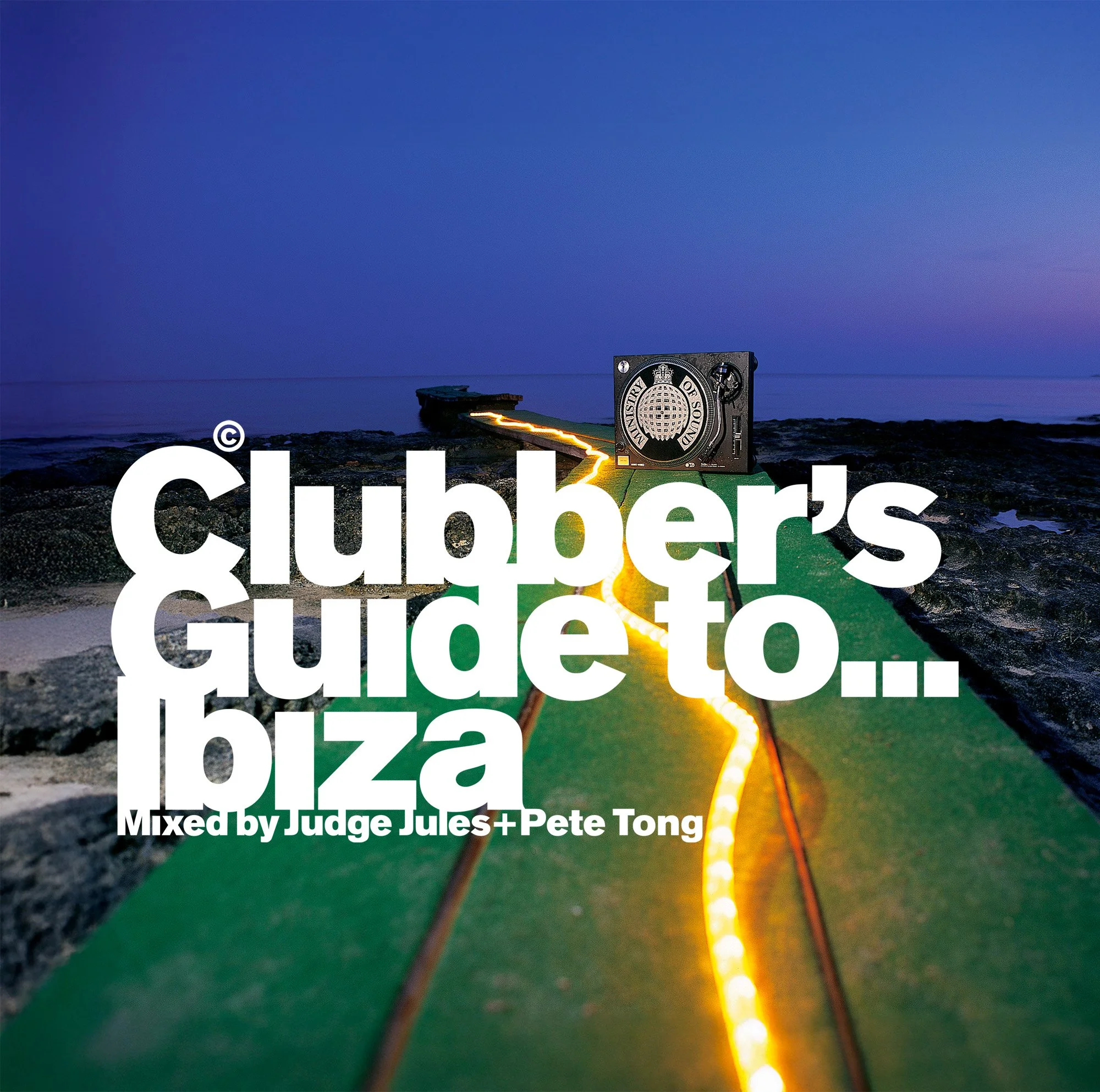 A DJ setup on a rocky beach at sunset or dusk with colorful sky, featuring a turntable, a green pathway with yellow lights, and large white text reading 'Clubber's guide to Ibiza' with smaller text 'Mixed by Judge Jules + Pete Tong'.