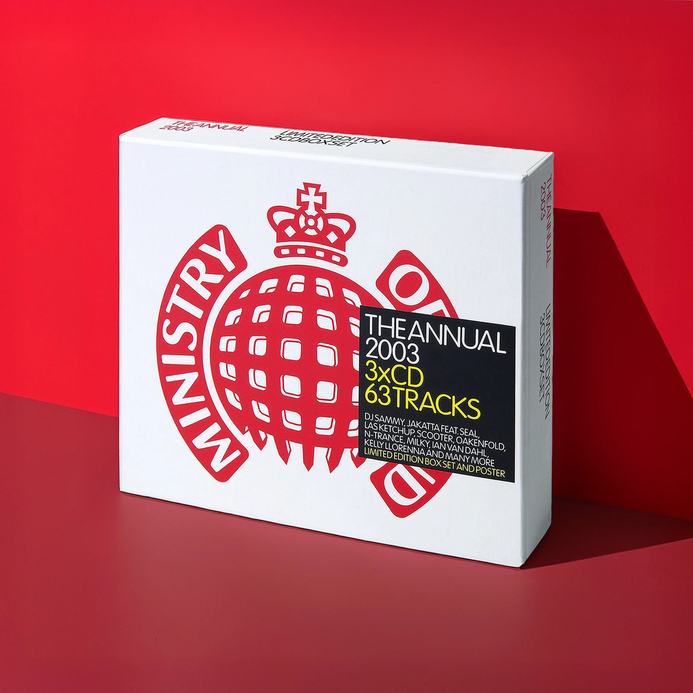 A box set of The Annual 2003 music compilation featuring 3 CDs and 63 tracks, with a white background and a large red logo of a crown atop a globe with wings. The box is placed on a red surface with red background lighting.
