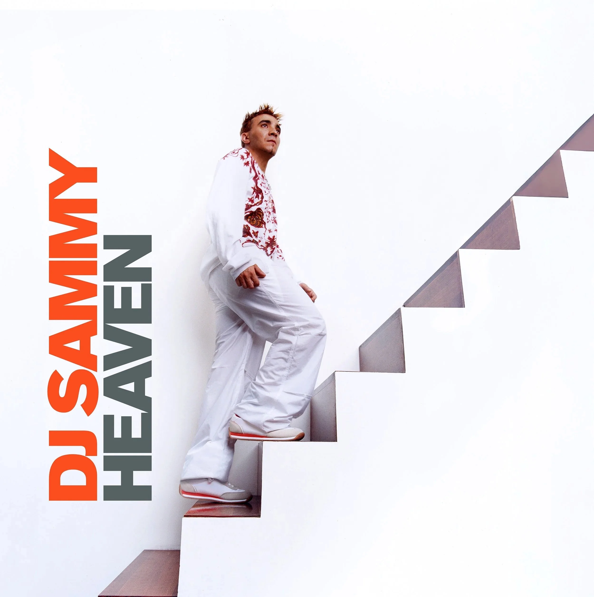 Man in white embroidered outfit standing on stairs with his foot on a higher step, looking upward, with the text 'DJ SANDY HEAVEN' written vertically on a white wall beside him.