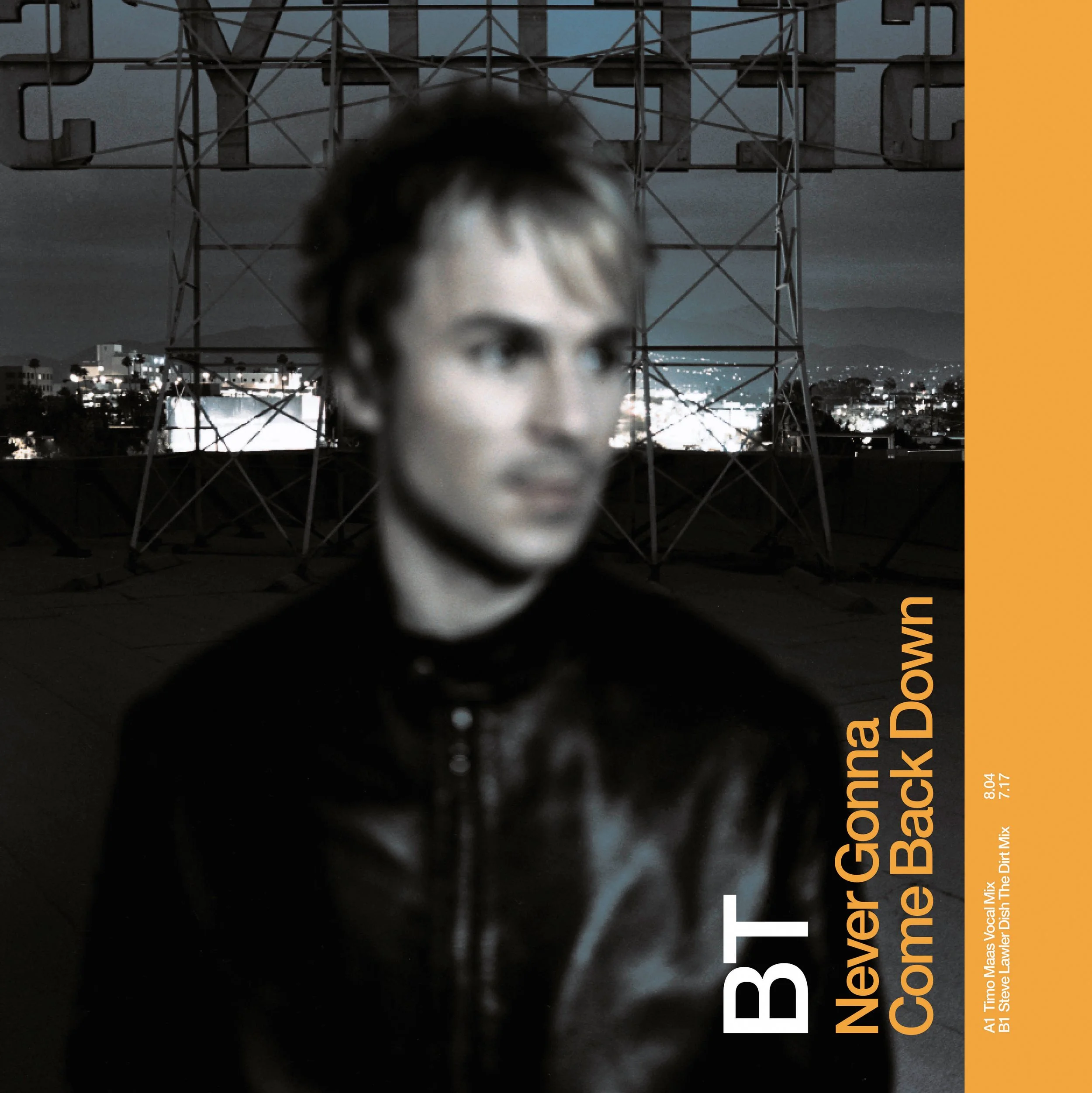 Blurred image of a man in a black leather jacket standing in front of a cityscape at night with a tower or power line structure behind him. There is orange text on the right side that reads, 'Never Gonna Come Back Down.'