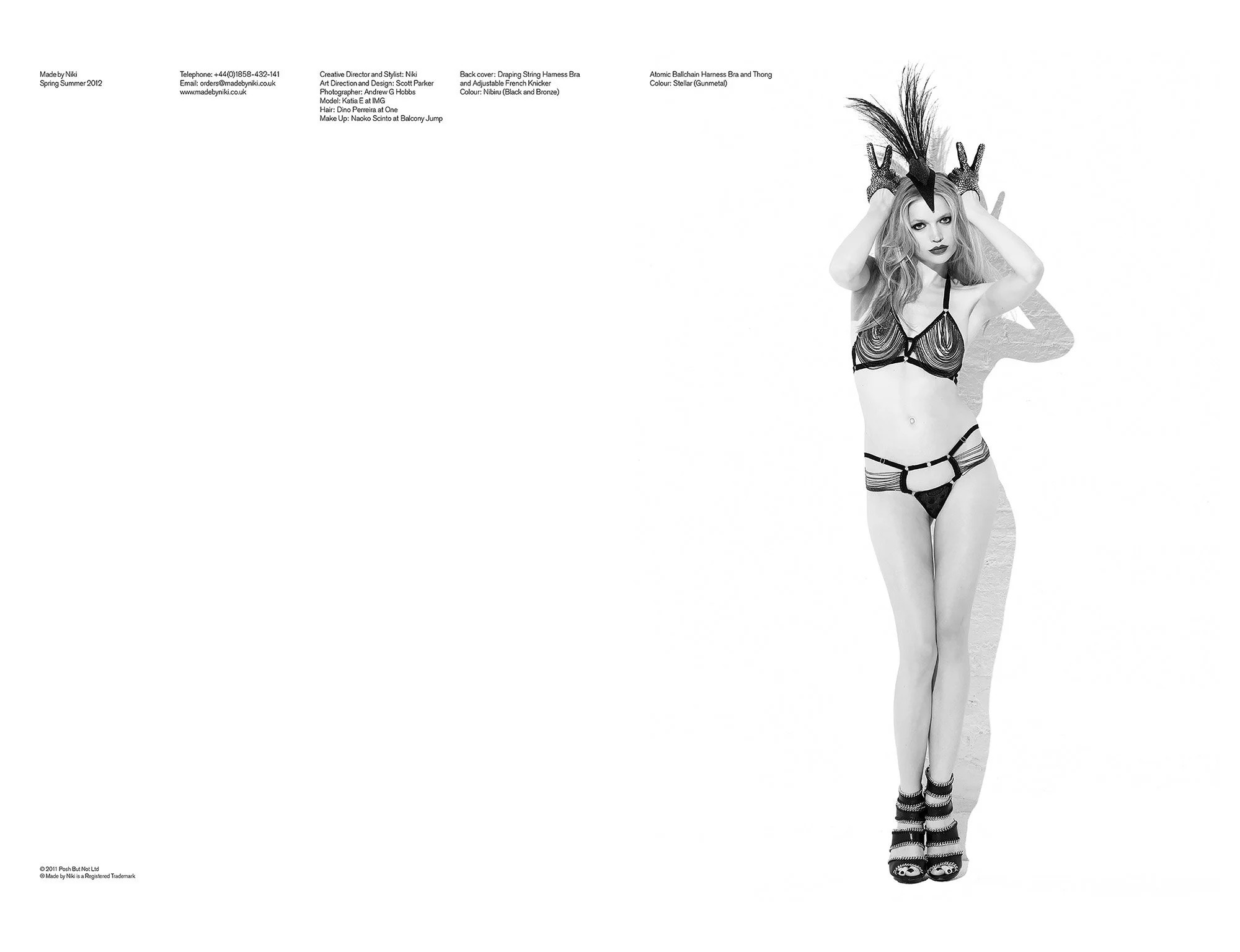 A woman with long hair in lingerie, wearing a headpiece with feathers and gloves, standing against a white background.