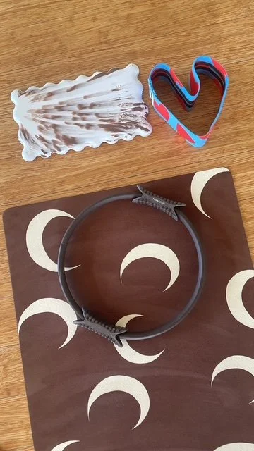 A knee pad, a blue and red heart patterned resistance band, and a brown mat with cream moon shapes on a wooden surface.