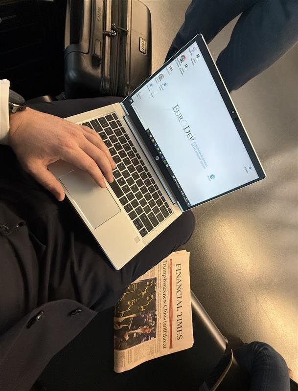 A man in a suit sitting down with a laptop, with the financial times next to him. Austria Airport in Vienna