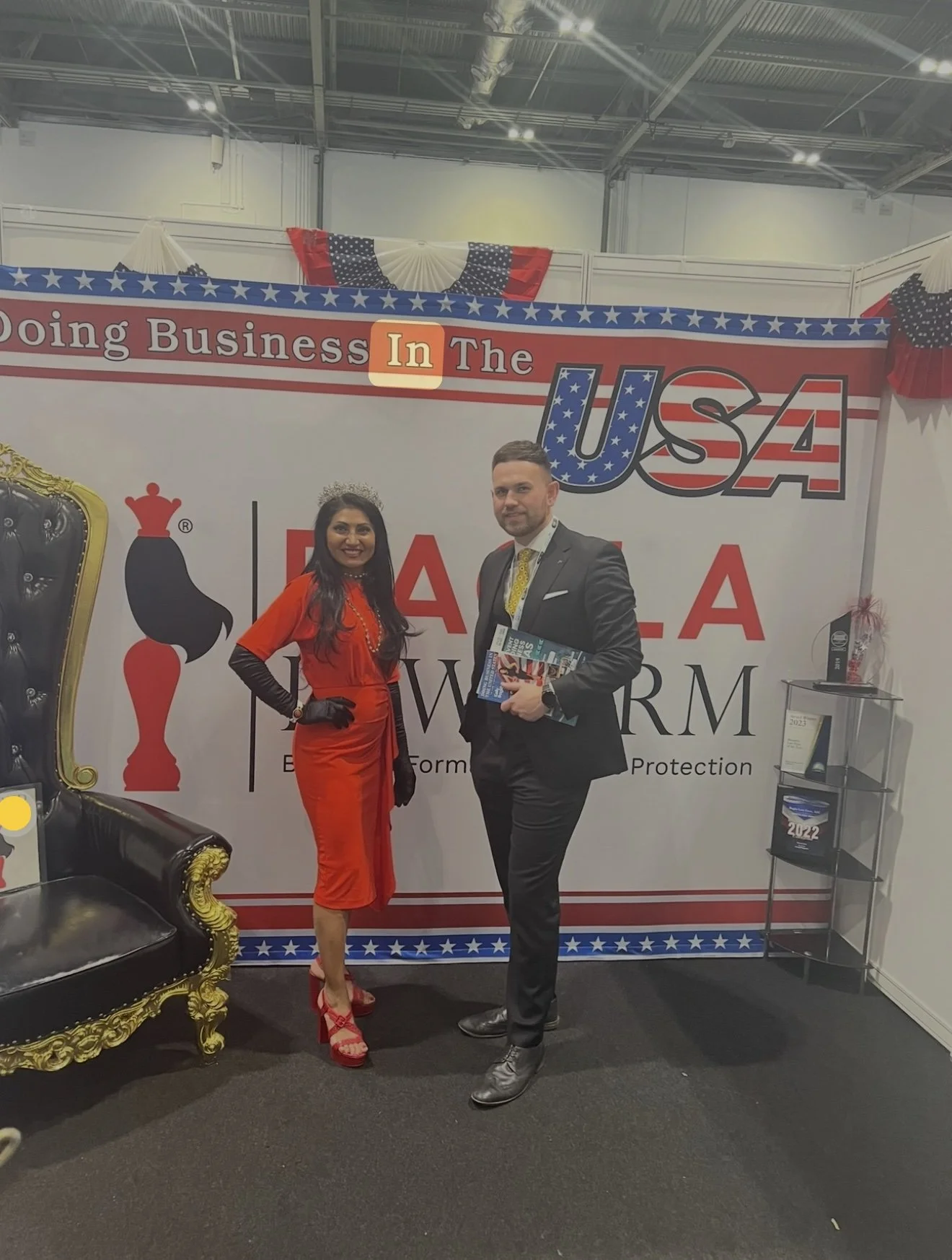 A woman in a red dress standing next to a man in a suit yellow tie, infront of a board that says doing business in the USA.
