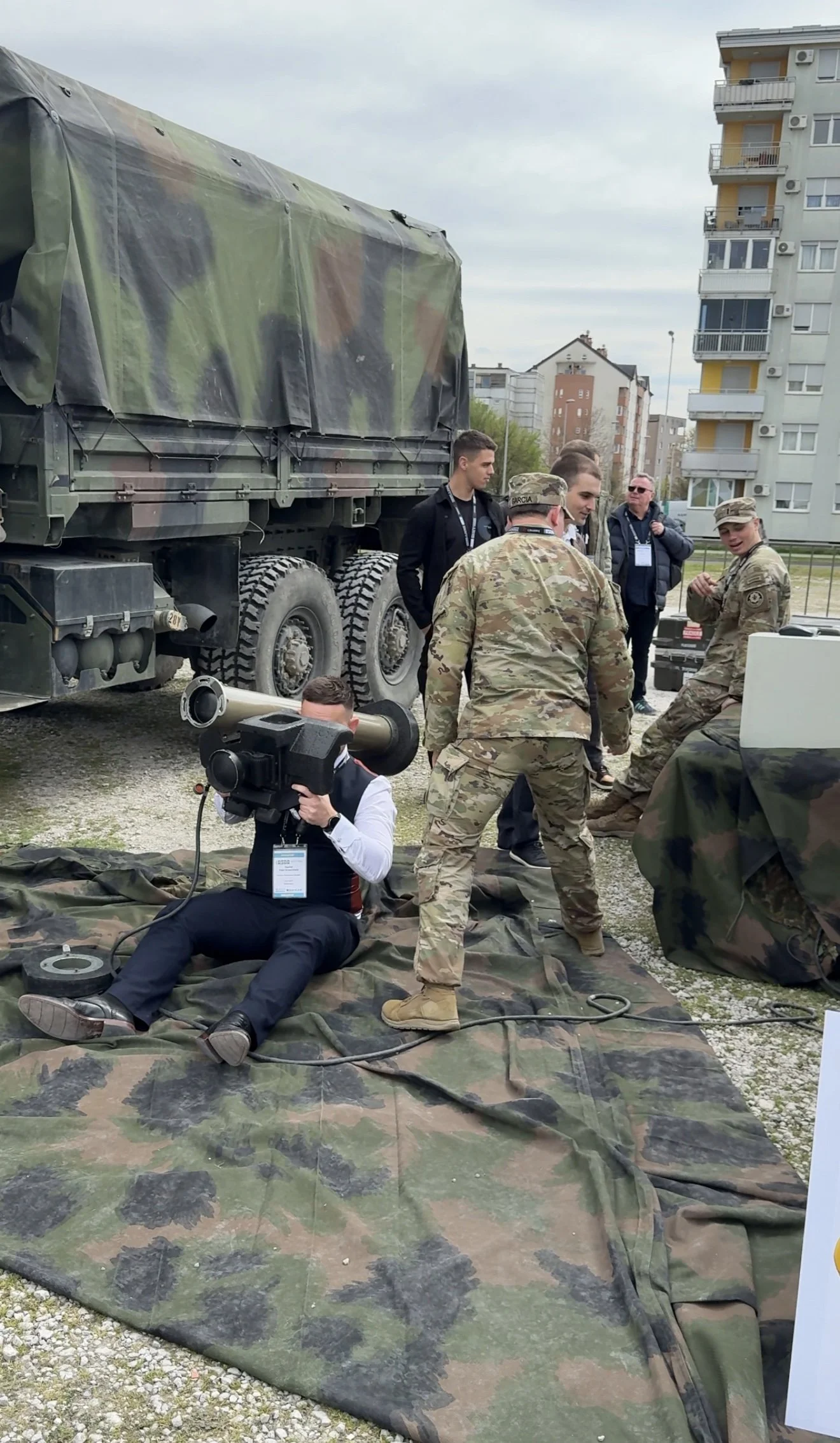 A man sat down next to a military truck with a Javelin or an Anti tank missile launcher  on his shoulder. Multiple US Marines stood next to him.