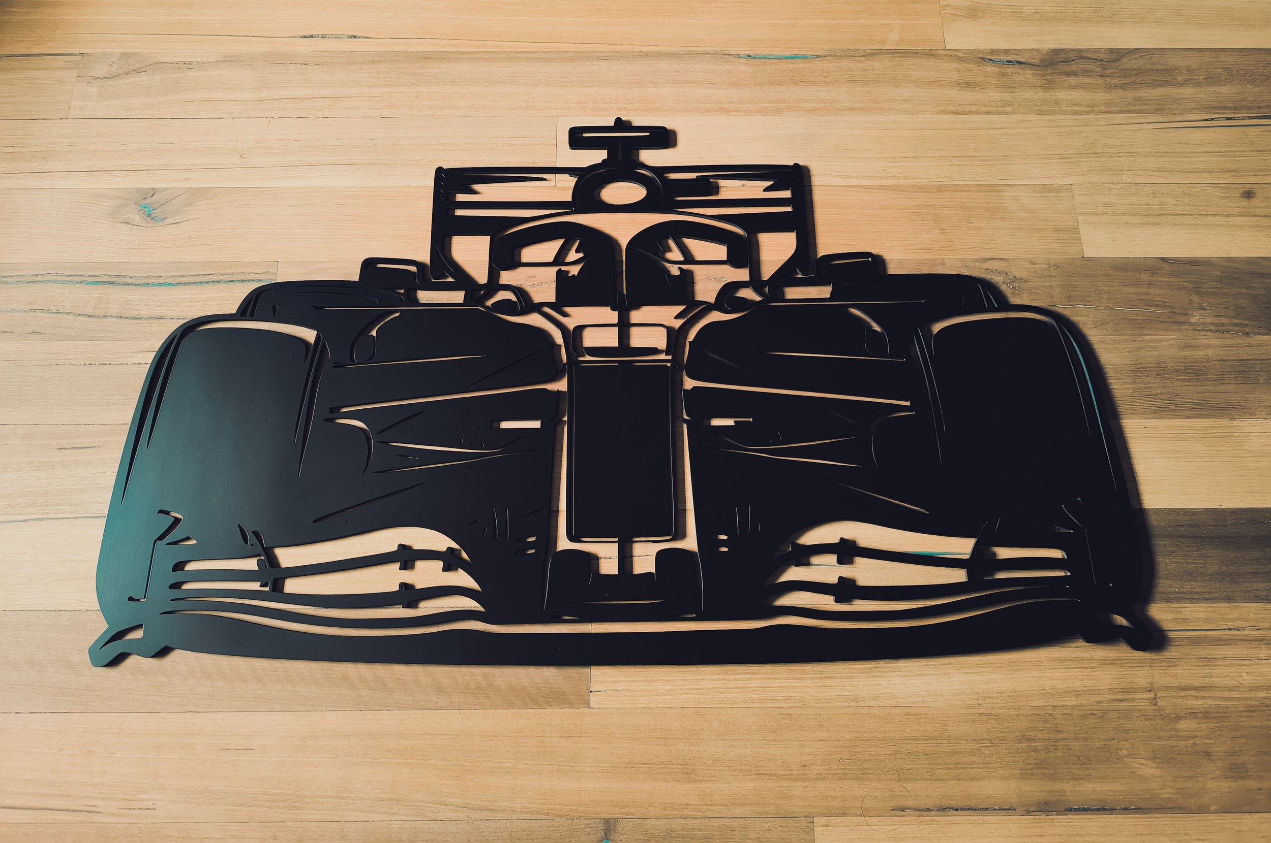 Front wing of a Formula 1 car made of black metal, placed on a wooden floor.