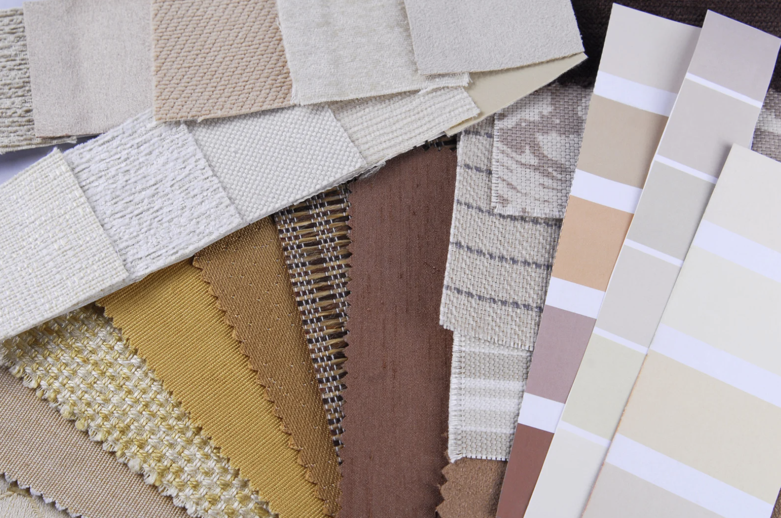 Échantillons de tissus et de revêtements dans des couleurs neutres et terre, disposés en couches pour une sélection de matériaux pour la décoration intérieure.