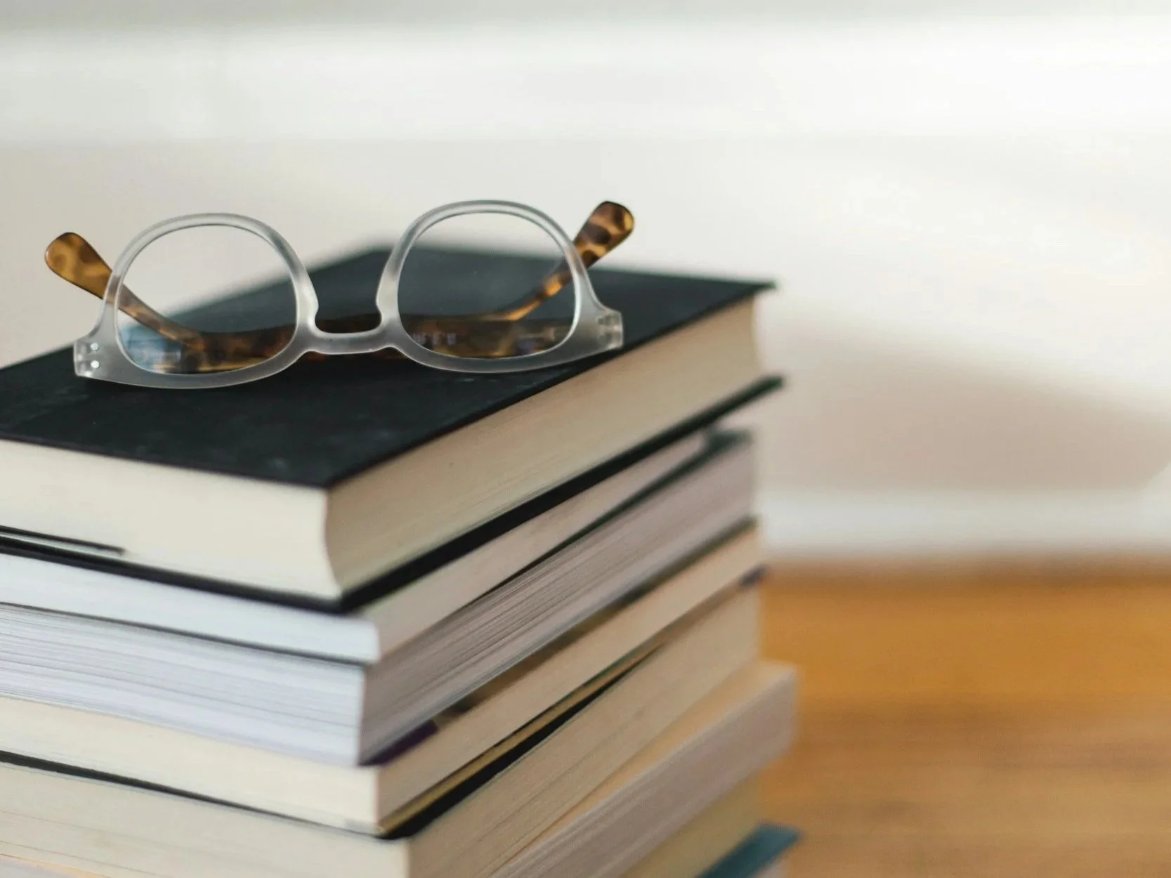 A stack of books with a pair of tortoiseshell glasses on top.