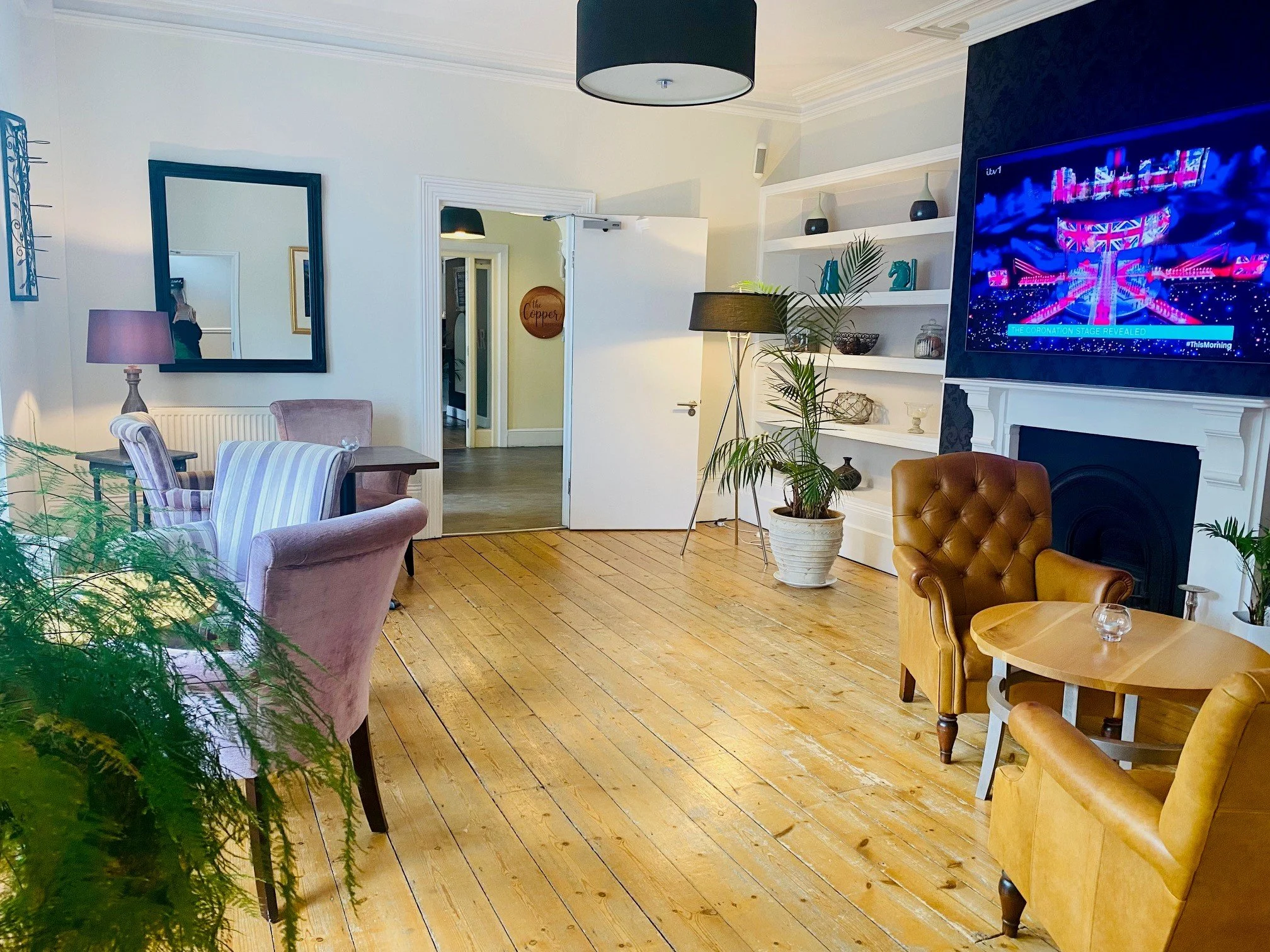 Hotel lounge with large television, comfortable seating, wooden floors and fire place