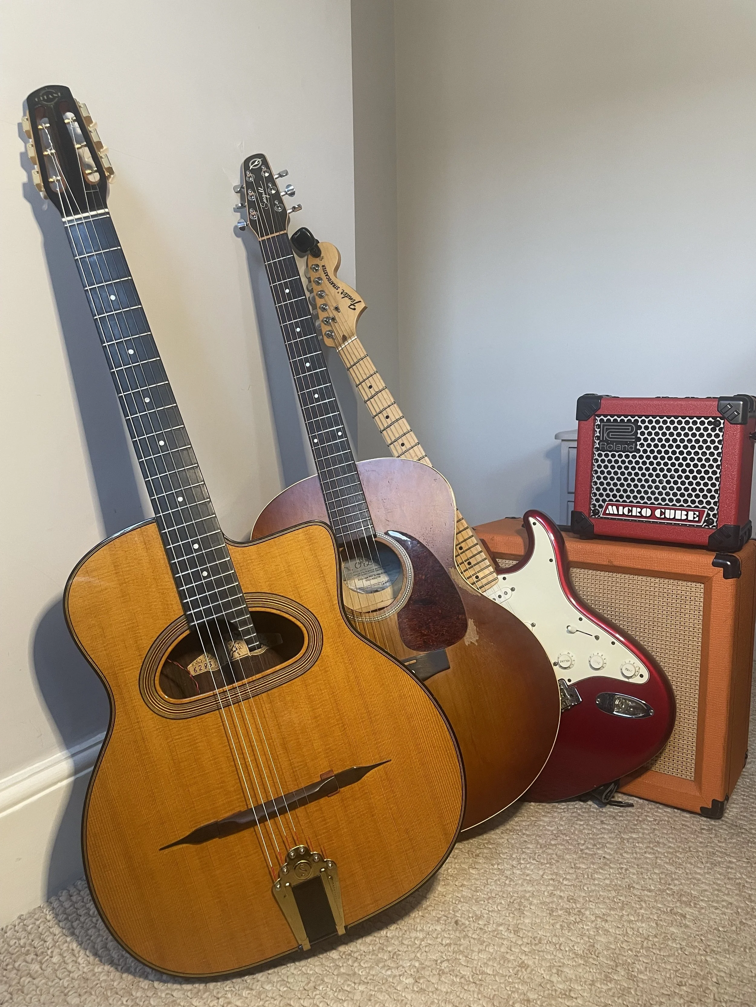 Two acoustic guitars and two electric guitars resting against a wall with small amplifiers on the floor.