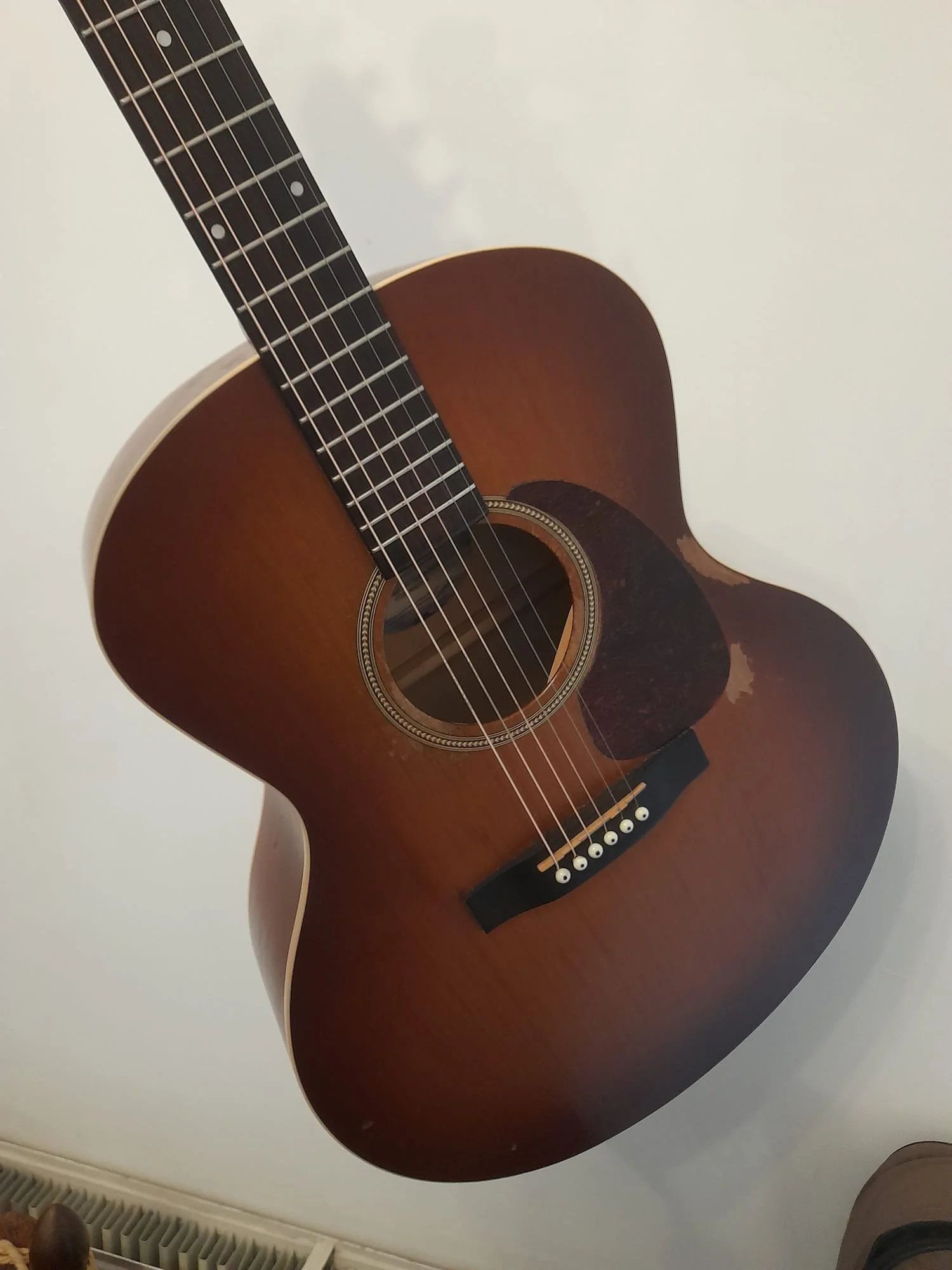 An acoustic guitar with a sunburst finish, six strings, black pickguard, and a round soundhole with decorative rosette.