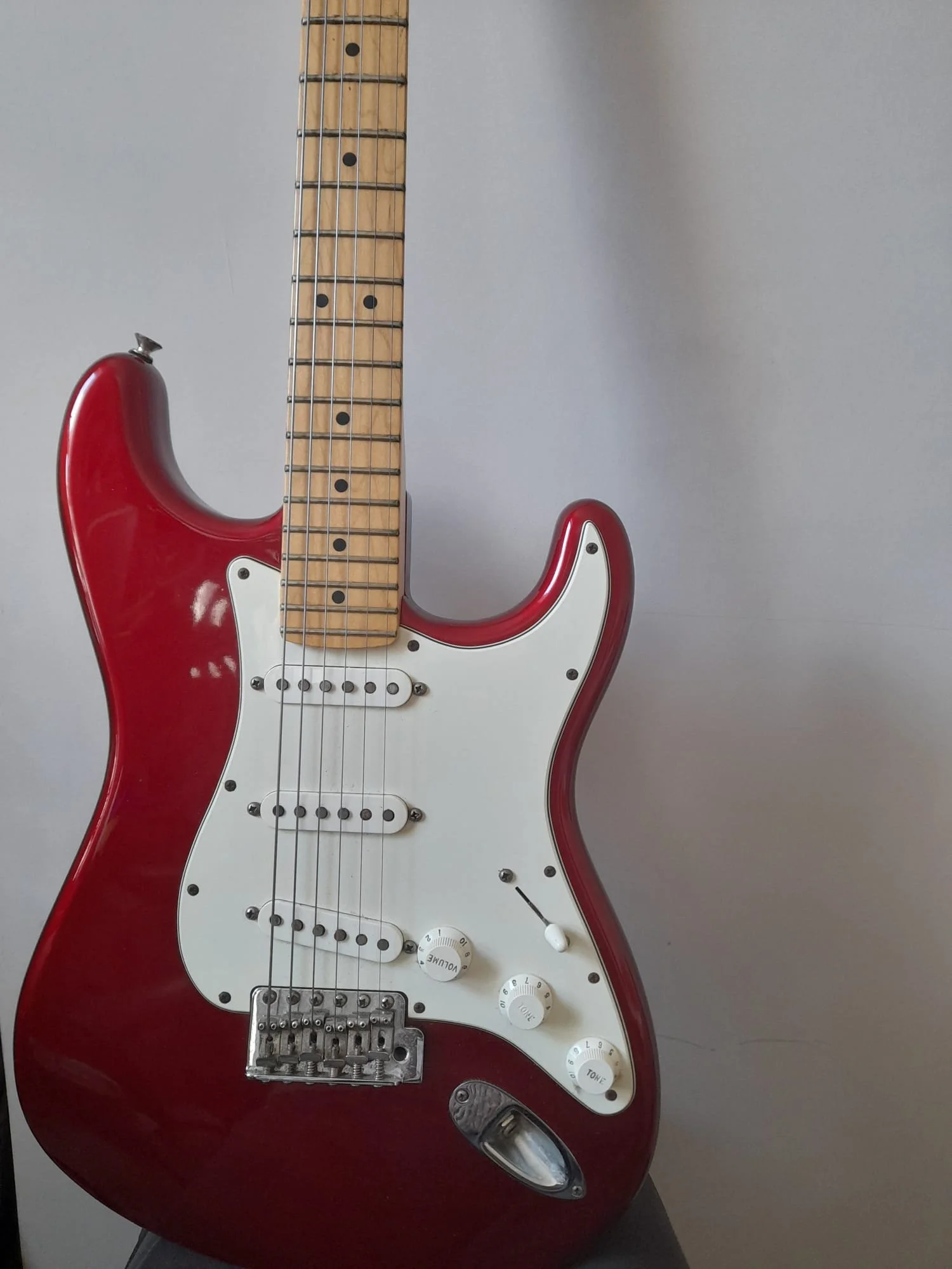 Red and white electric guitar with a maple neck, mounted against a plain wall.