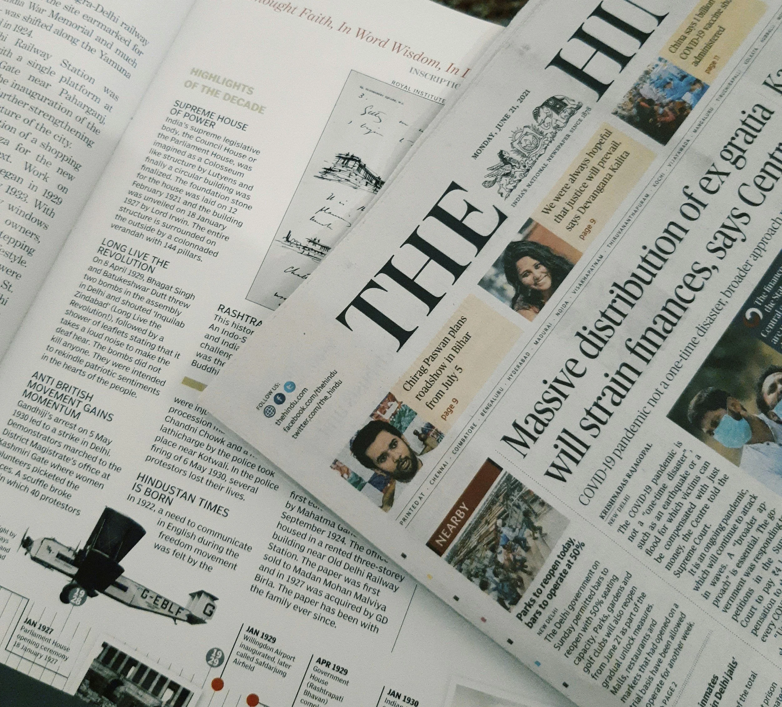 Close-up of newspapers with text, images, and advertisements, including headlines about history, politics, and cultural topics.