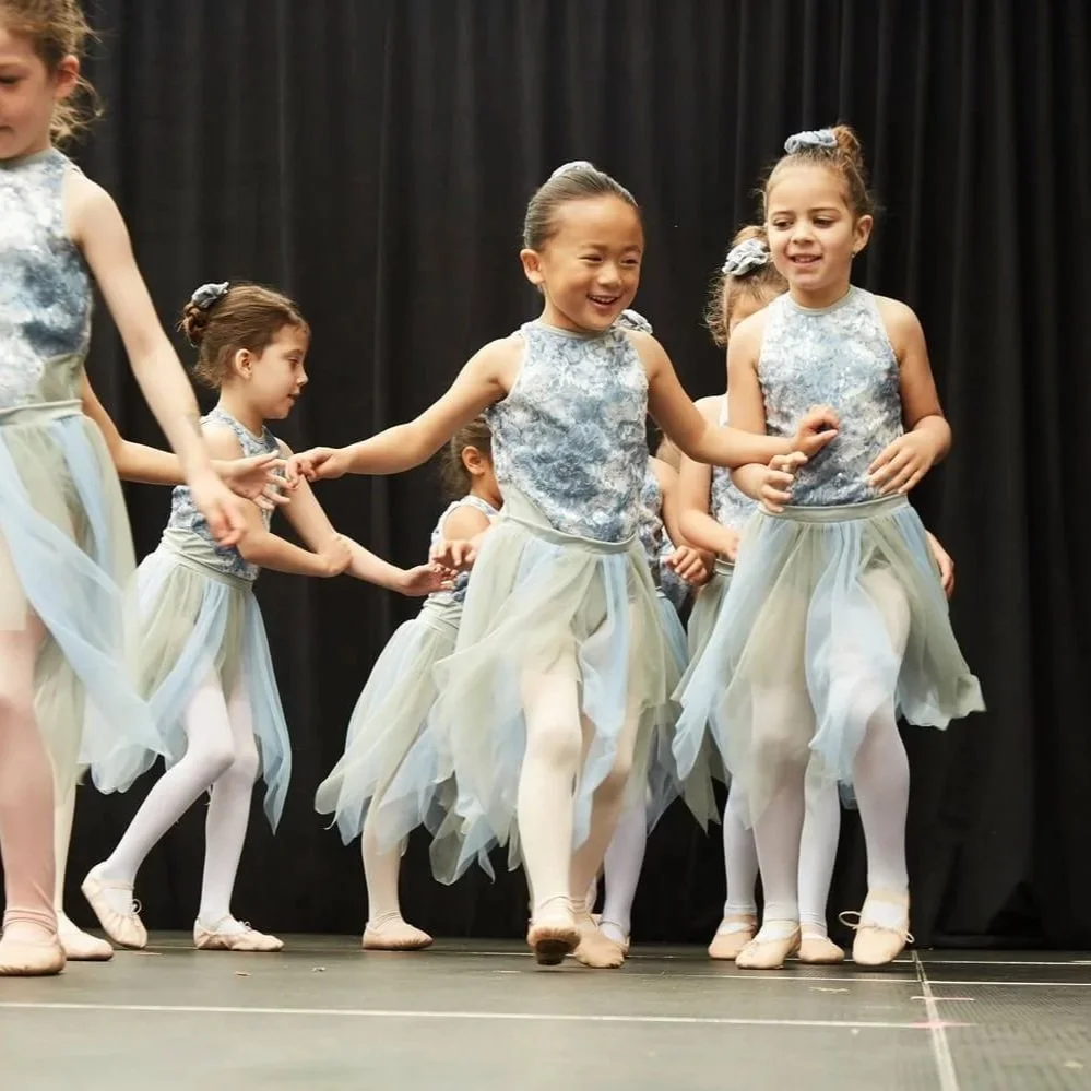 Group of young girls in ballet costumes performing on stage during their Dance with Miss Alice recital.