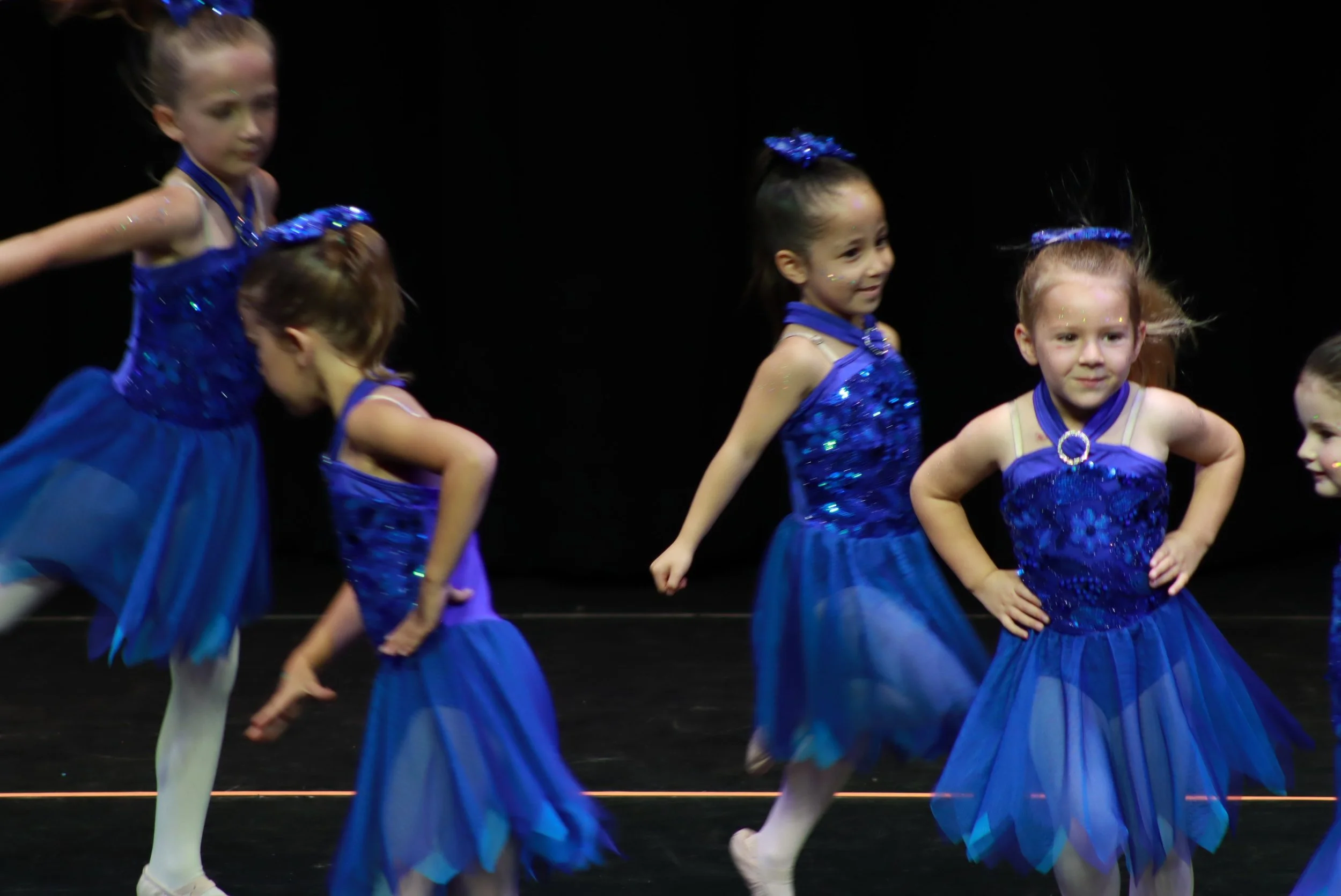 Young girls in blue dance costumes performing on stage.