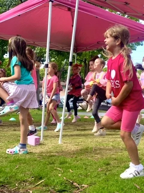 Children playing on swings under a pink canopy at an outdoor event.