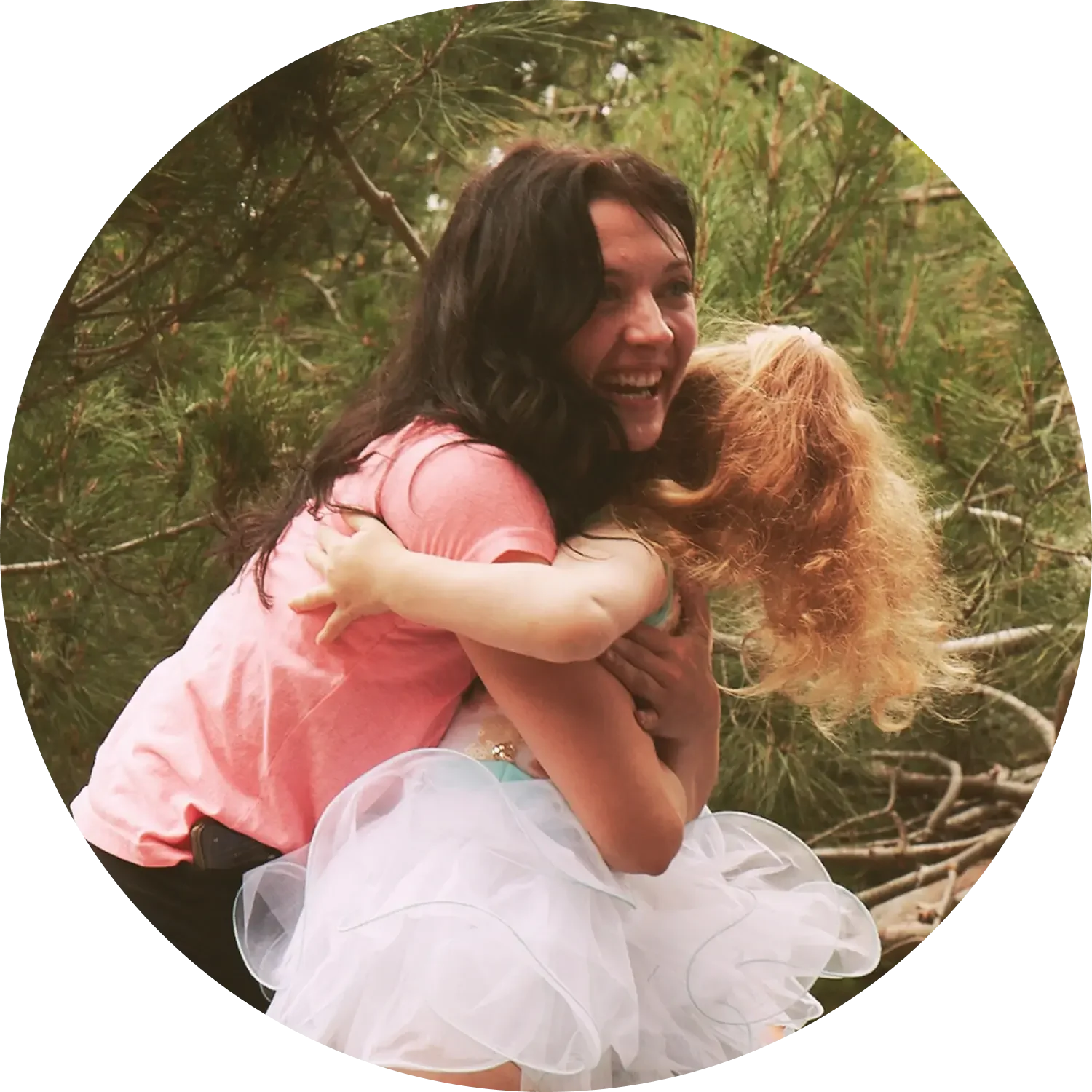 Miss Isa of Dance with Miss Alice, hugging a young student outdoors amidst trees, both smiling and showing affection.