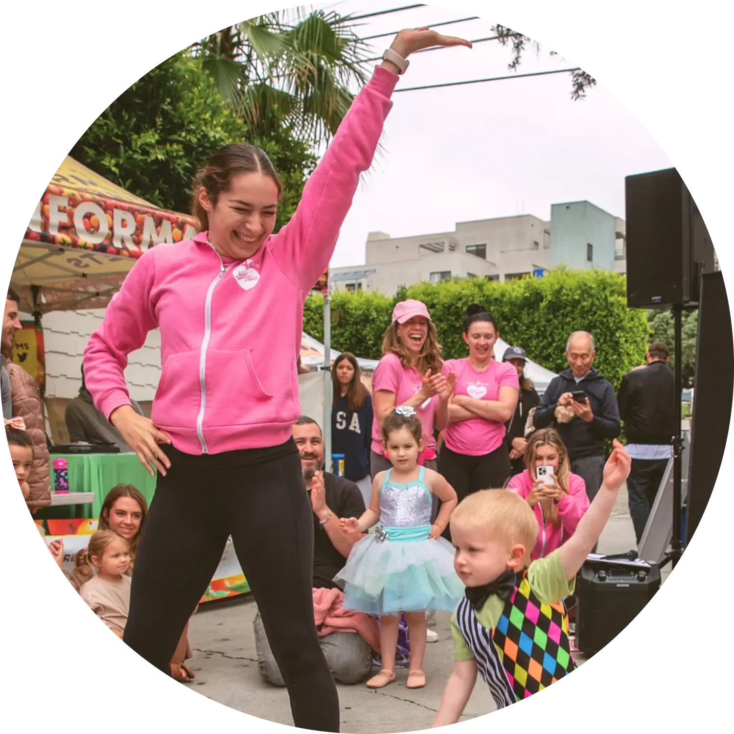 Miss Ashton in a pink hoodie and black leggings dances with a young boy with blond hair and colorful argyle shirt at a Dance with Miss Alice event.
