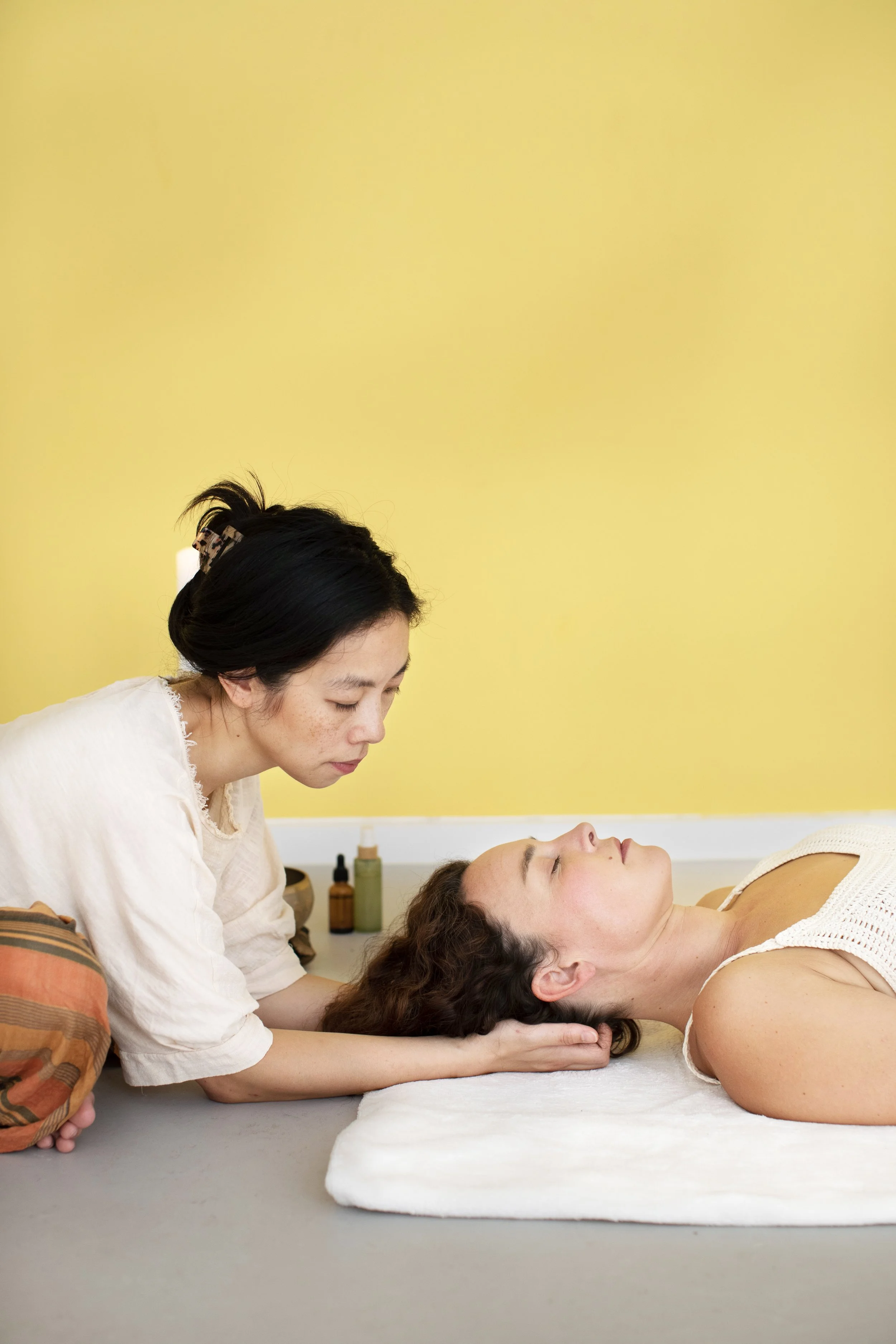 A woman receiving a gentle massage from a practitioner in a relaxing setting with skincare products in the background.